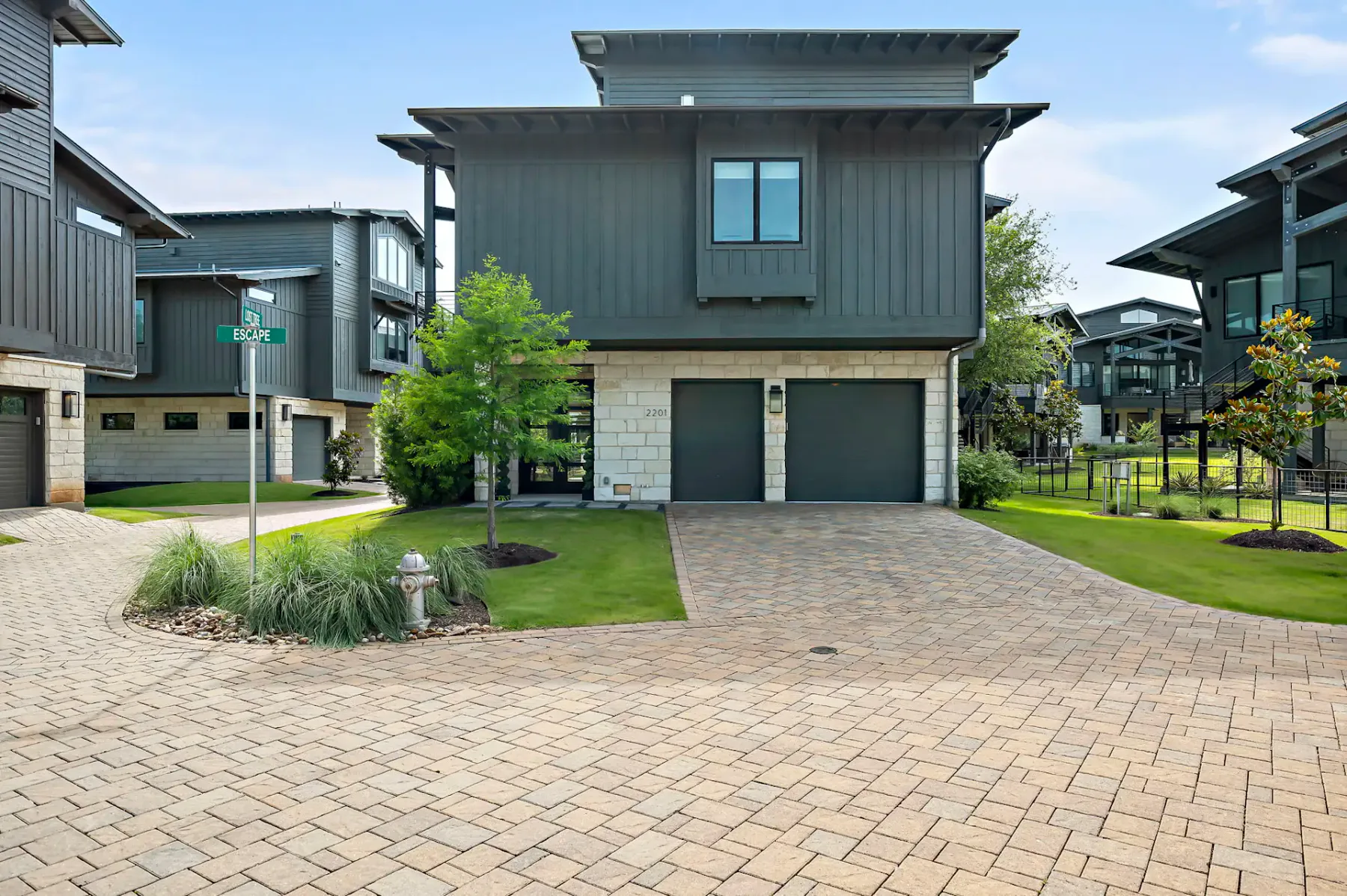 Modern home with gray siding, a garage, and a paved driveway beside landscaped lawns.