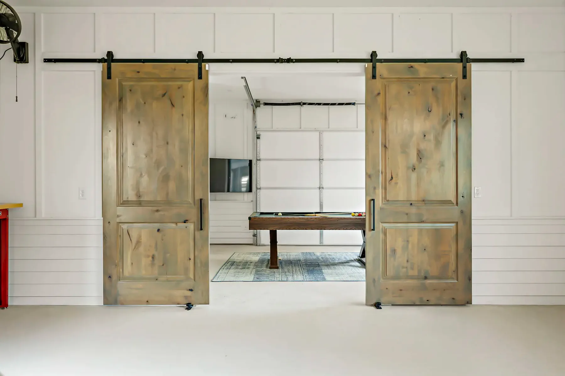Open wooden sliding doors reveal a pool table in a bright room.
