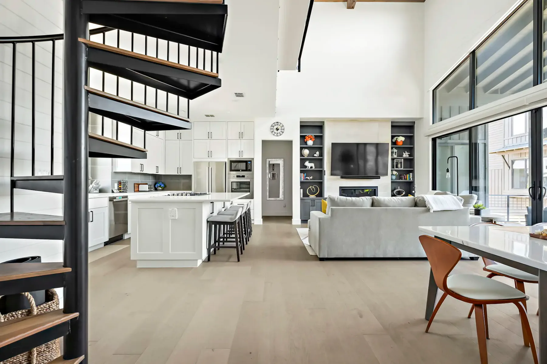 Open-plan living room and kitchen with a dining table beside large windows.