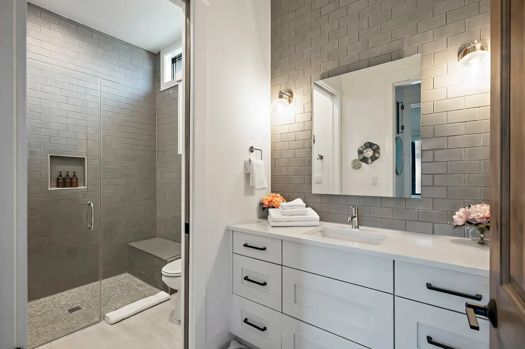 A tiled bathroom with a glass shower and a white vanity with two sinks.