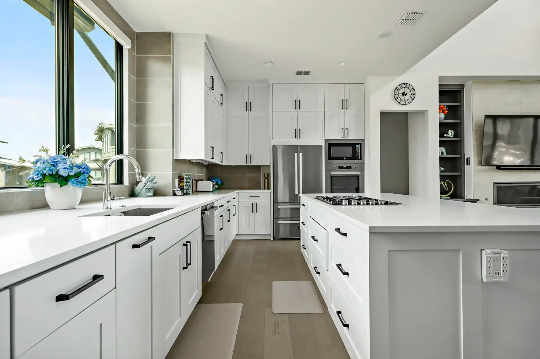 Modern kitchen with white cabinets, island with cooktop, stainless steel appliances, large window, and light wood flooring.