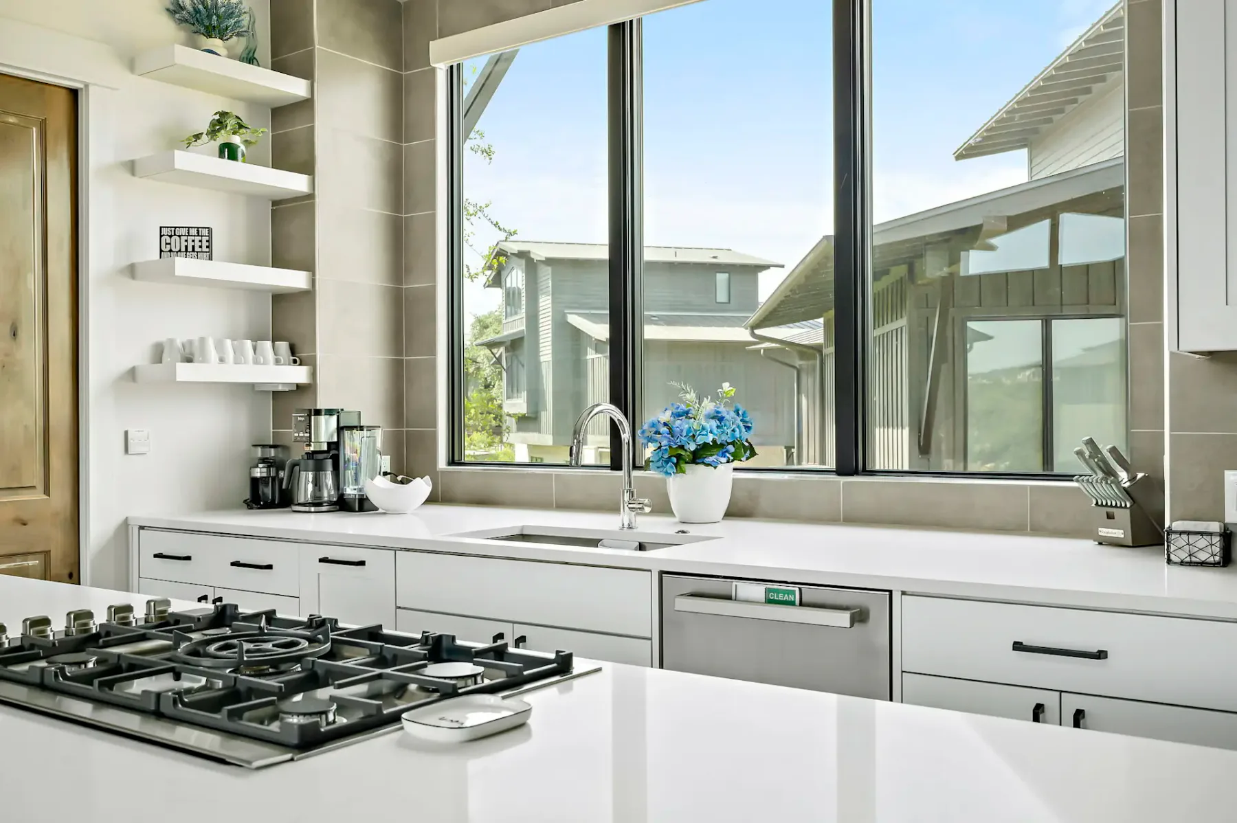 A bright kitchen with a cooktop, sink, and large windows overlooking nearby buildings.