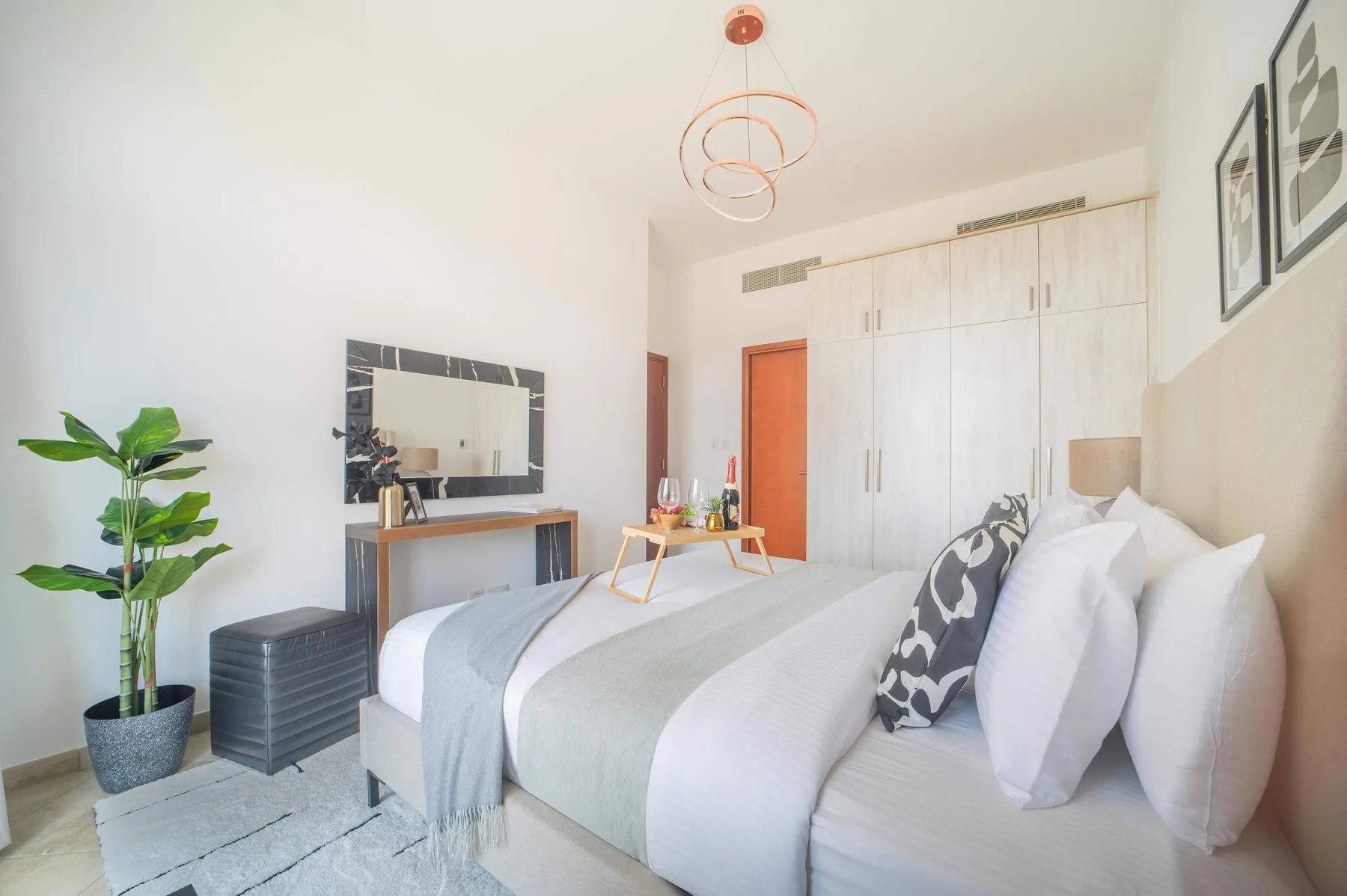 Un dormitorio luminoso con una cama tendida y un escritorio junto al espejo de pared.