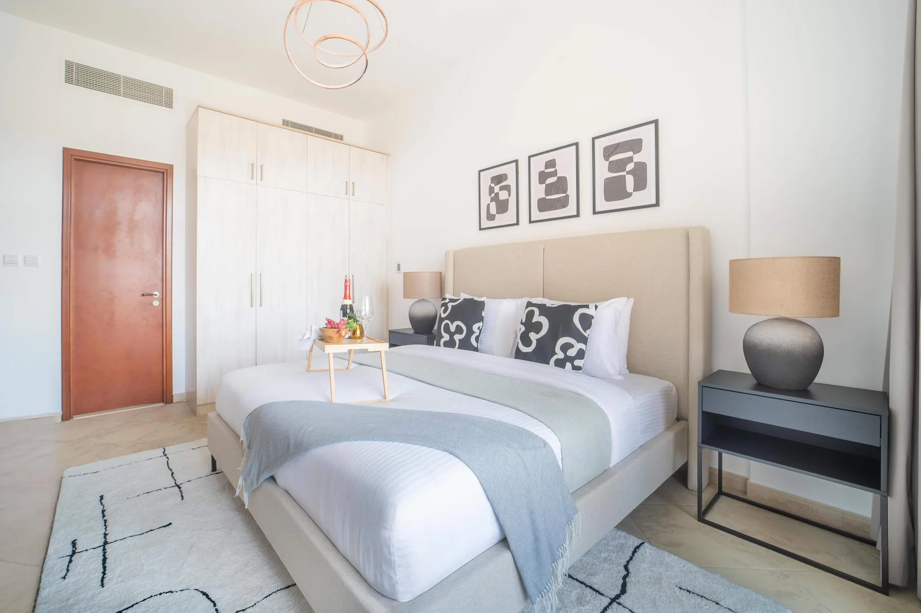Un dormitorio luminoso con una cama, mesitas de noche y cuadros enmarcados.