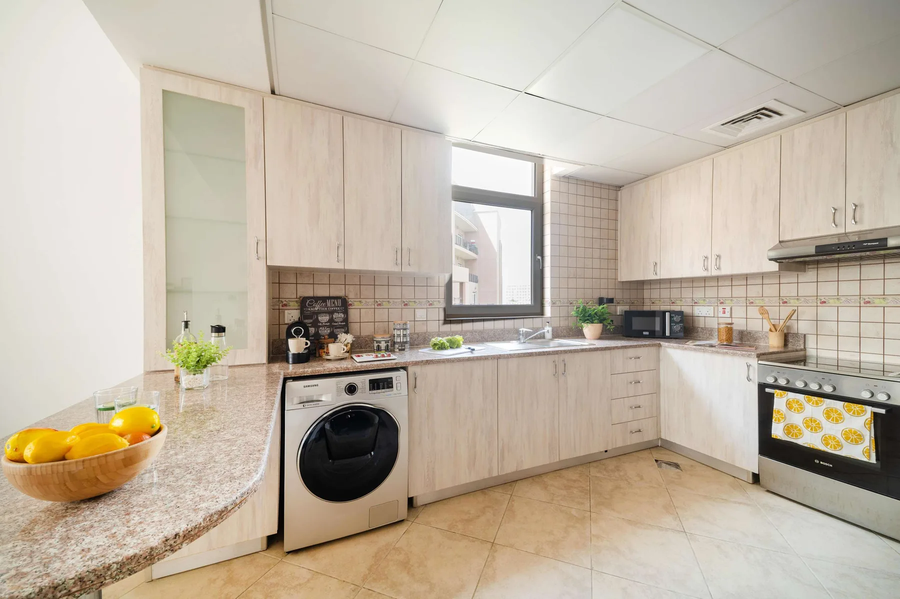 Una cocina luminosa con gabinetes de madera clara y una lavadora.