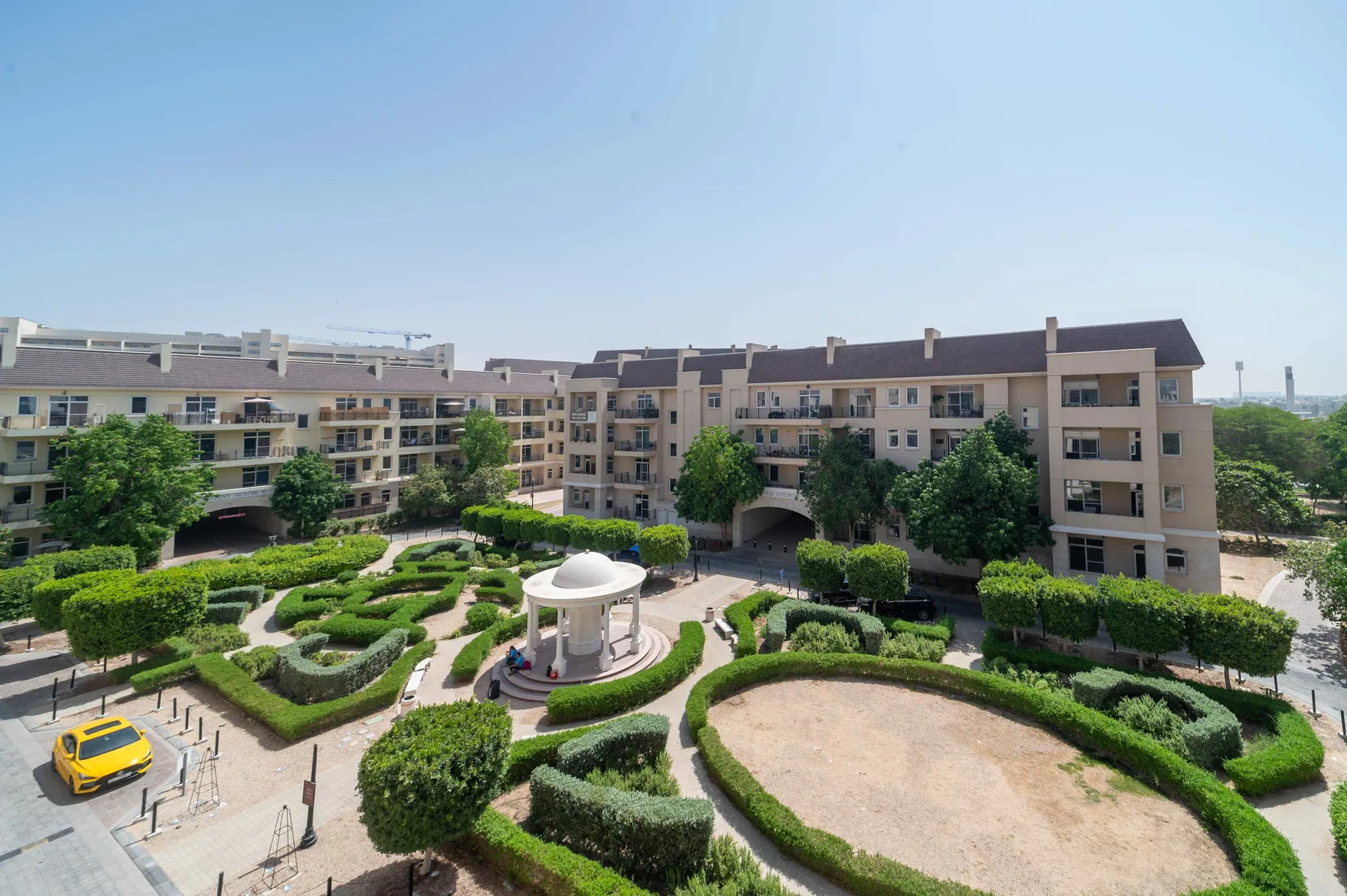 Un patio ajardinado con senderos sinuosos y una fuente circular entre edificios de apartamentos.