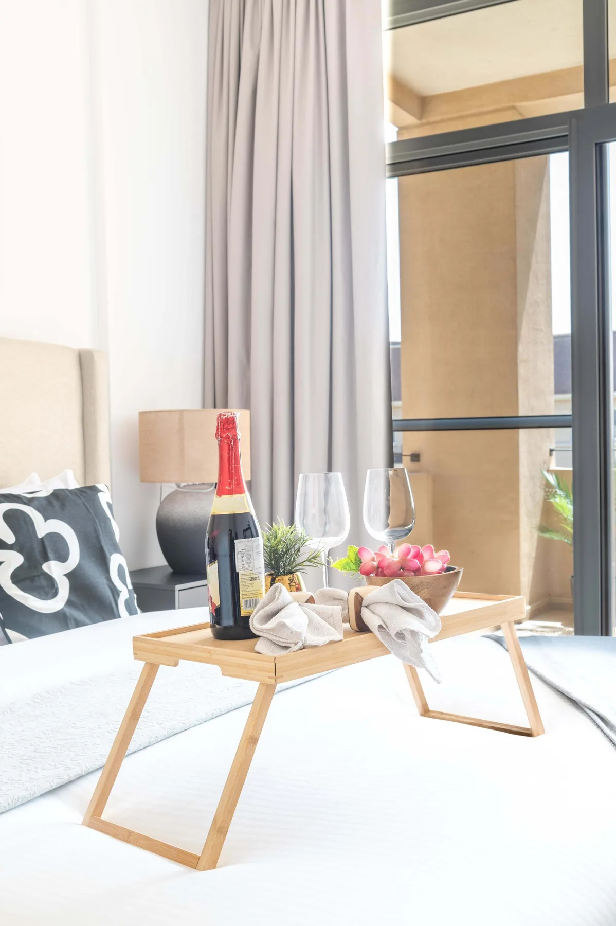 Un dormitorio luminoso con una bandeja baja de madera con bebidas y flores sobre la cama.