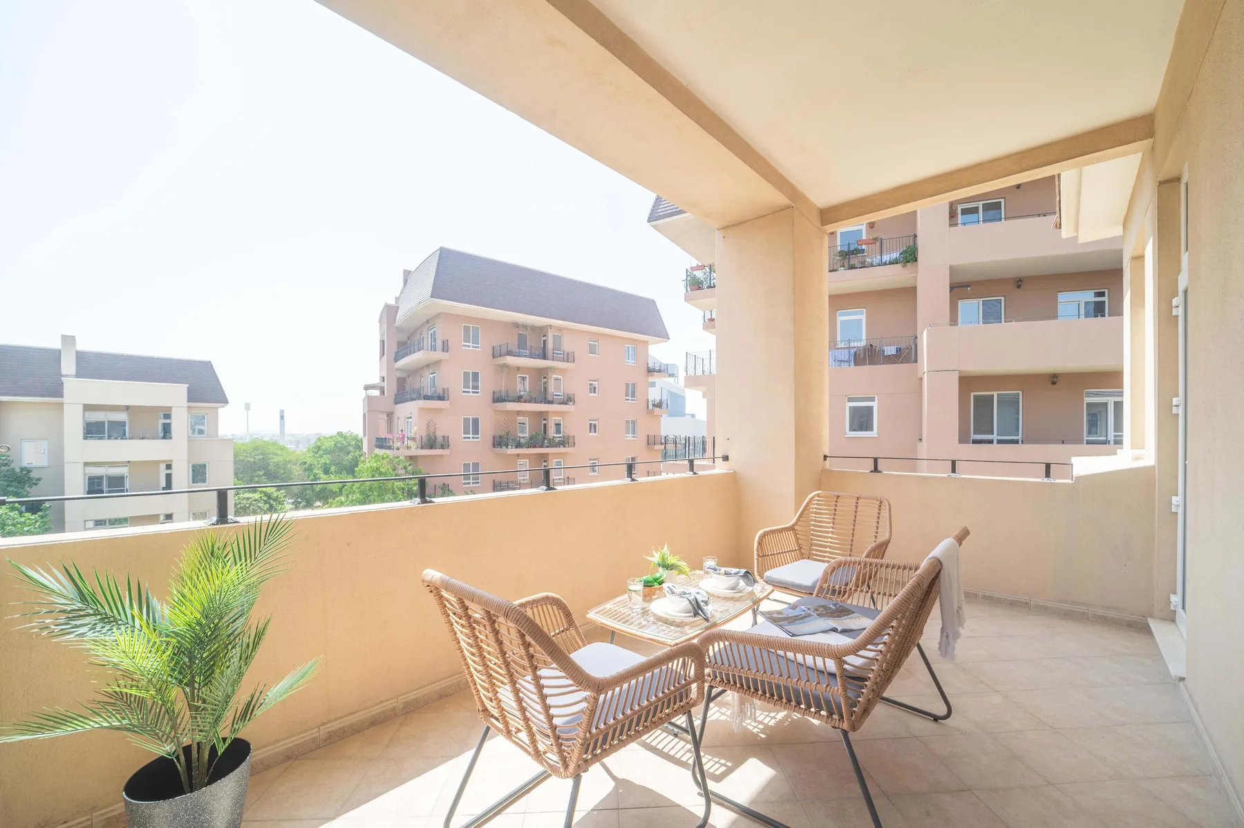 Un balcón cubierto con asientos de mimbre y una mesa pequeña da a edificios de apartamentos vecinos.