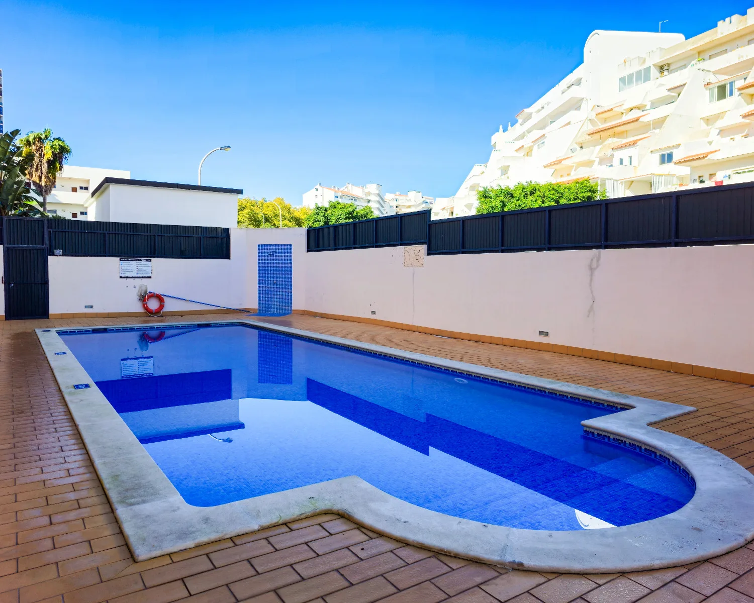 An outdoor swimming pool is surrounded by a tiled deck and boundary walls.