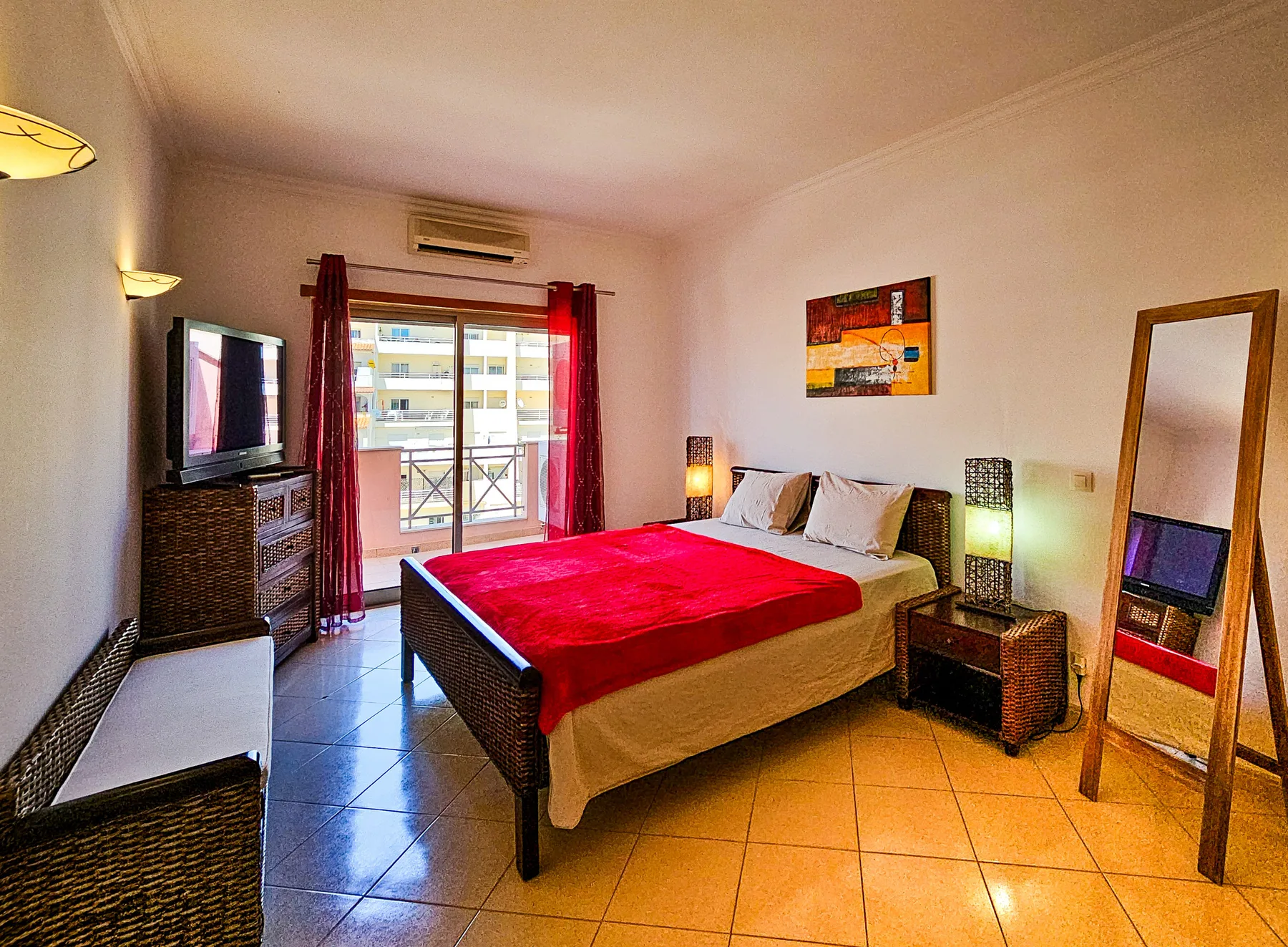 A bedroom with a large bed, red bedspread, and balcony doors.