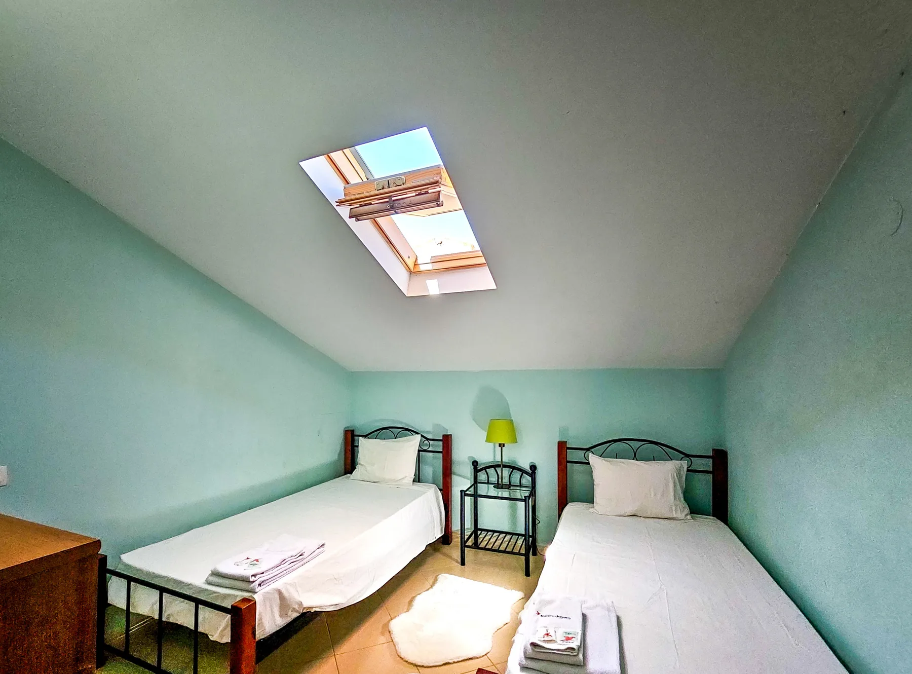 A bedroom with two single beds beneath a skylight.