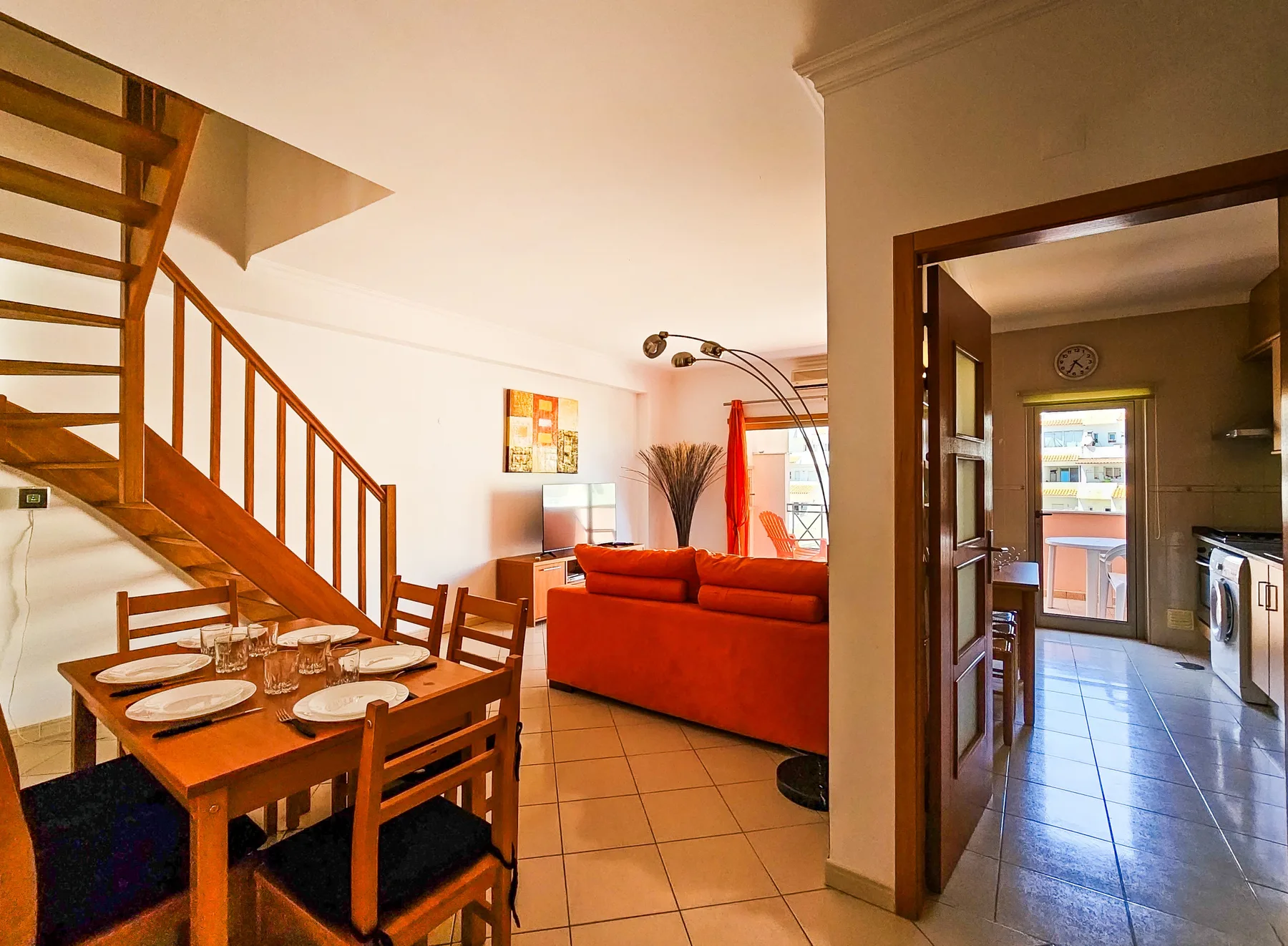 A bright living and dining area with a staircase and an orange sofa.