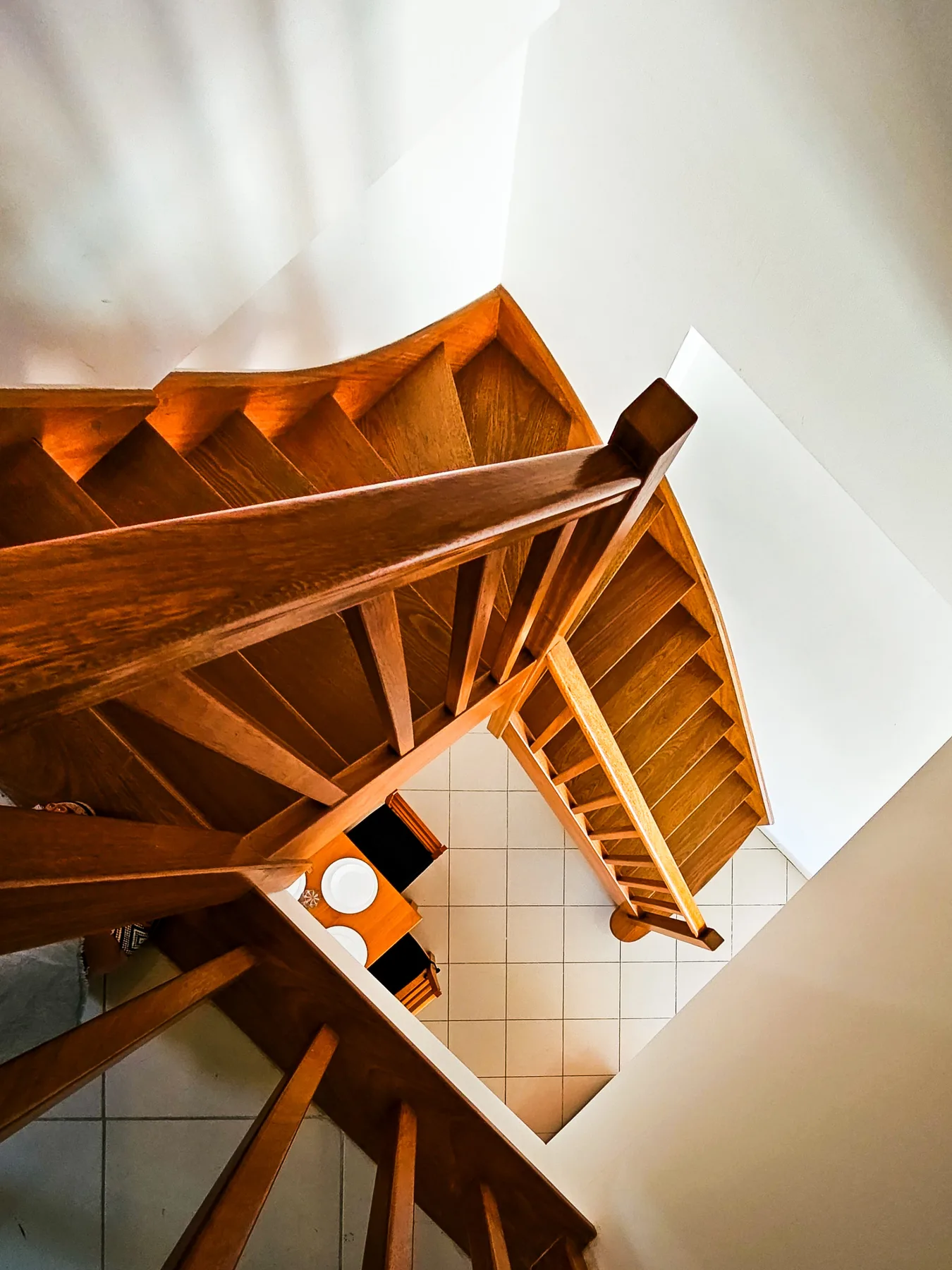 Una escalera de madera rodea una barandilla central sobre un suelo de baldosas.