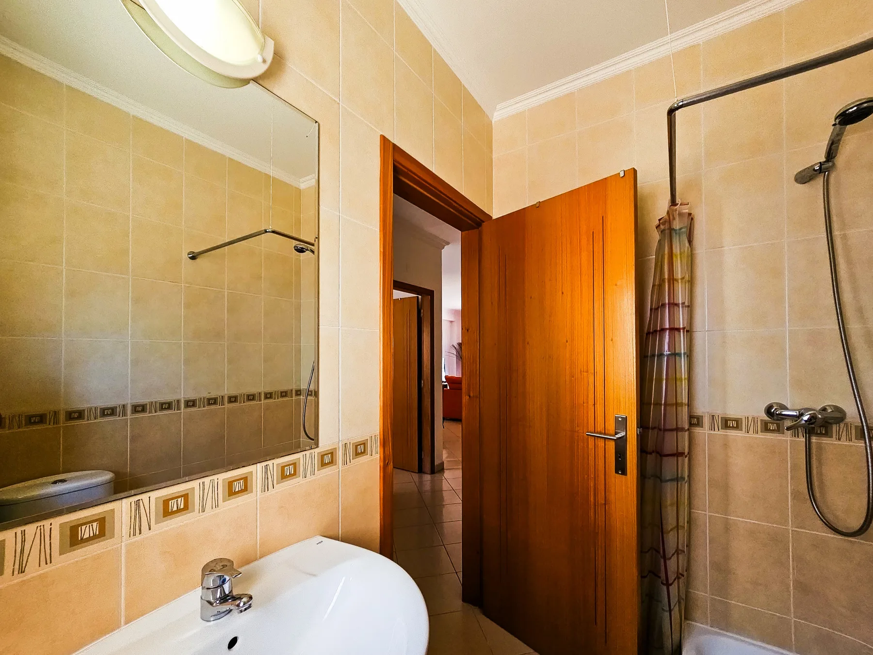 Un baño alicatado con lavabo, espejo y ducha.