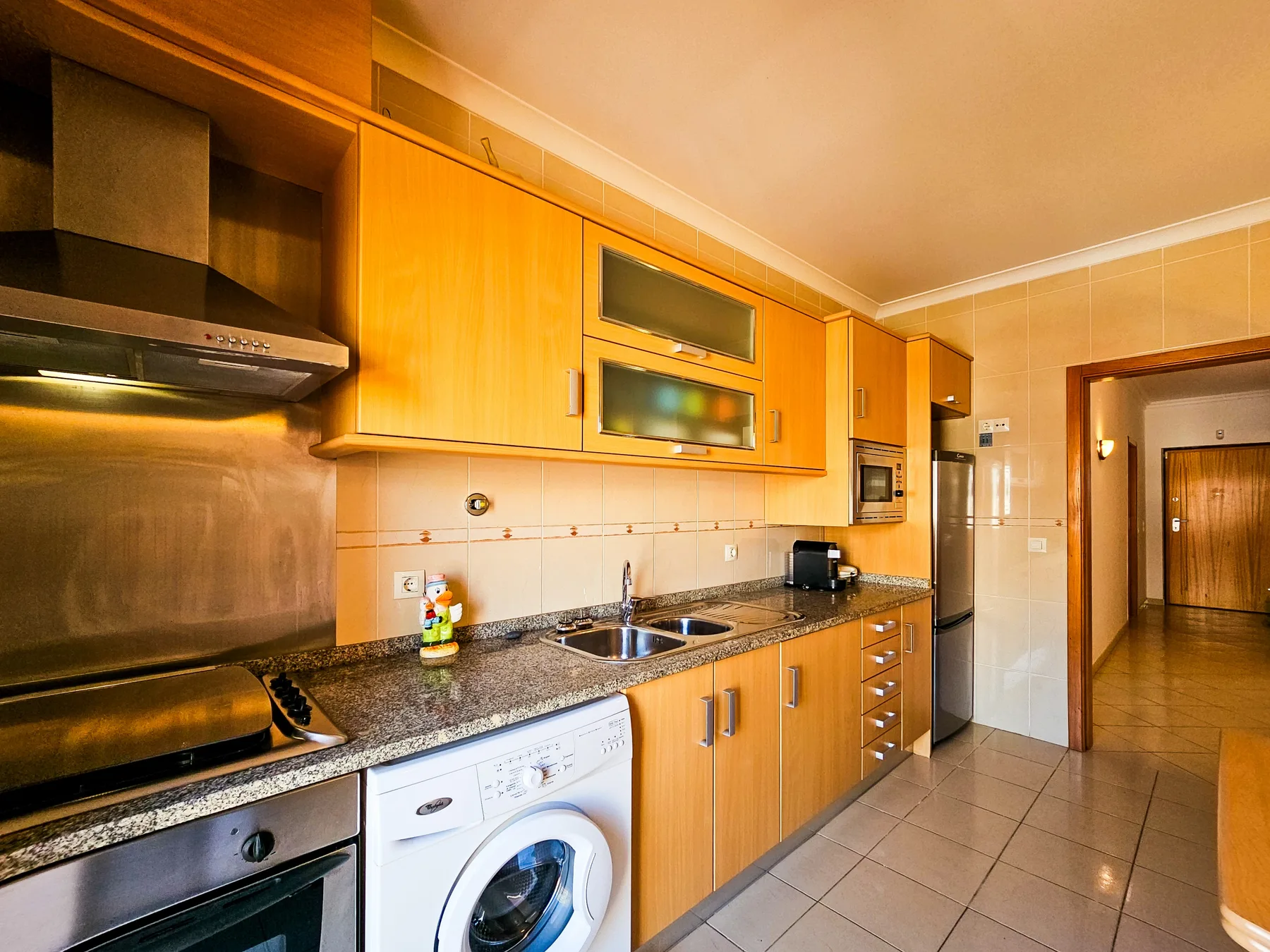 A kitchen with wooden cabinets, a cooktop, sink, and washing machine.