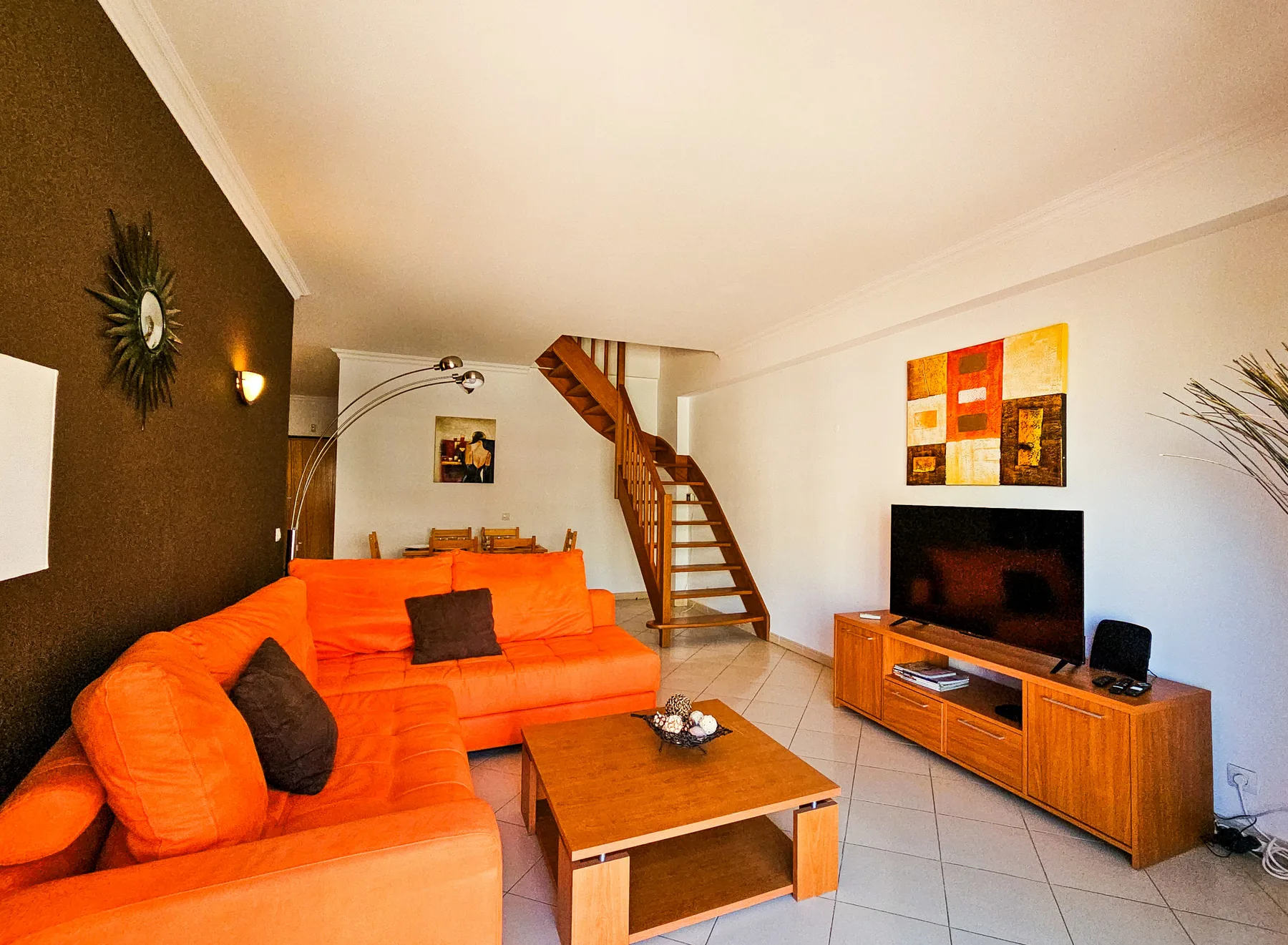Living room with orange seating, a television, and a staircase.