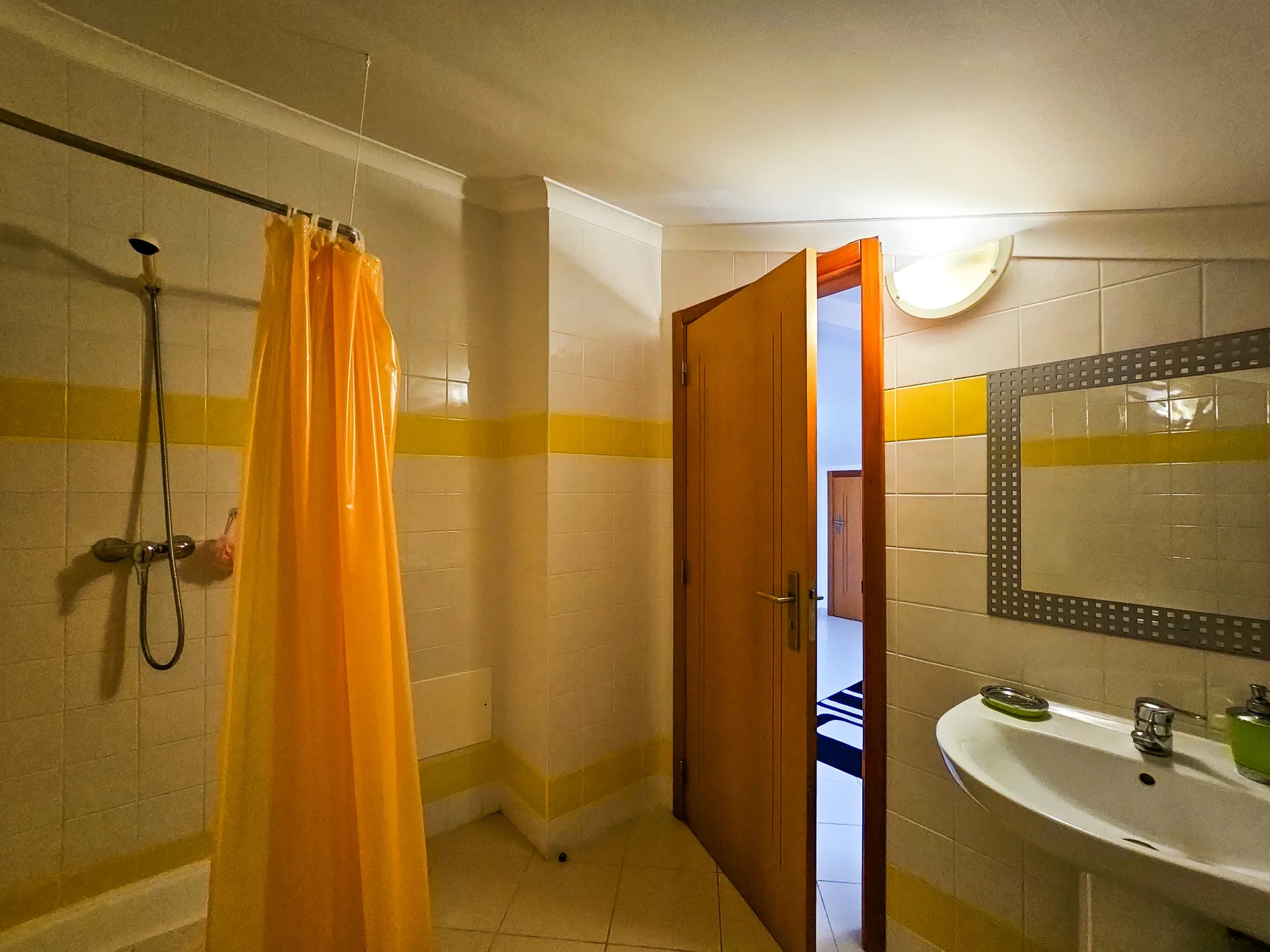 A tiled bathroom with a shower curtain, sink, and open door.