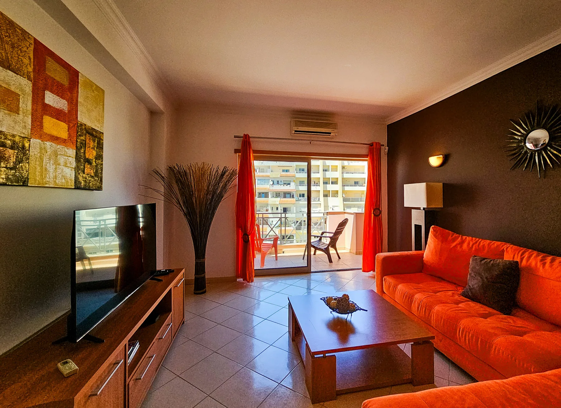 A living room with orange seating and a coffee table beside the balcony doors.