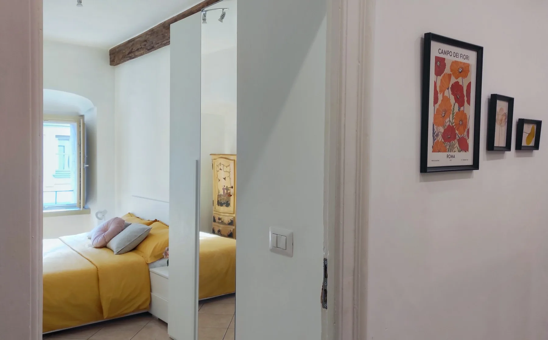 Un dormitorio con una cama amarilla, una ventana y cuadros en el pasillo contiguo.
