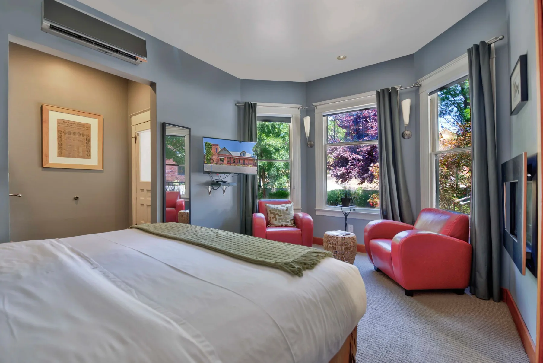 Bedroom with a large bed, sitting area, and windows overlooking trees.
