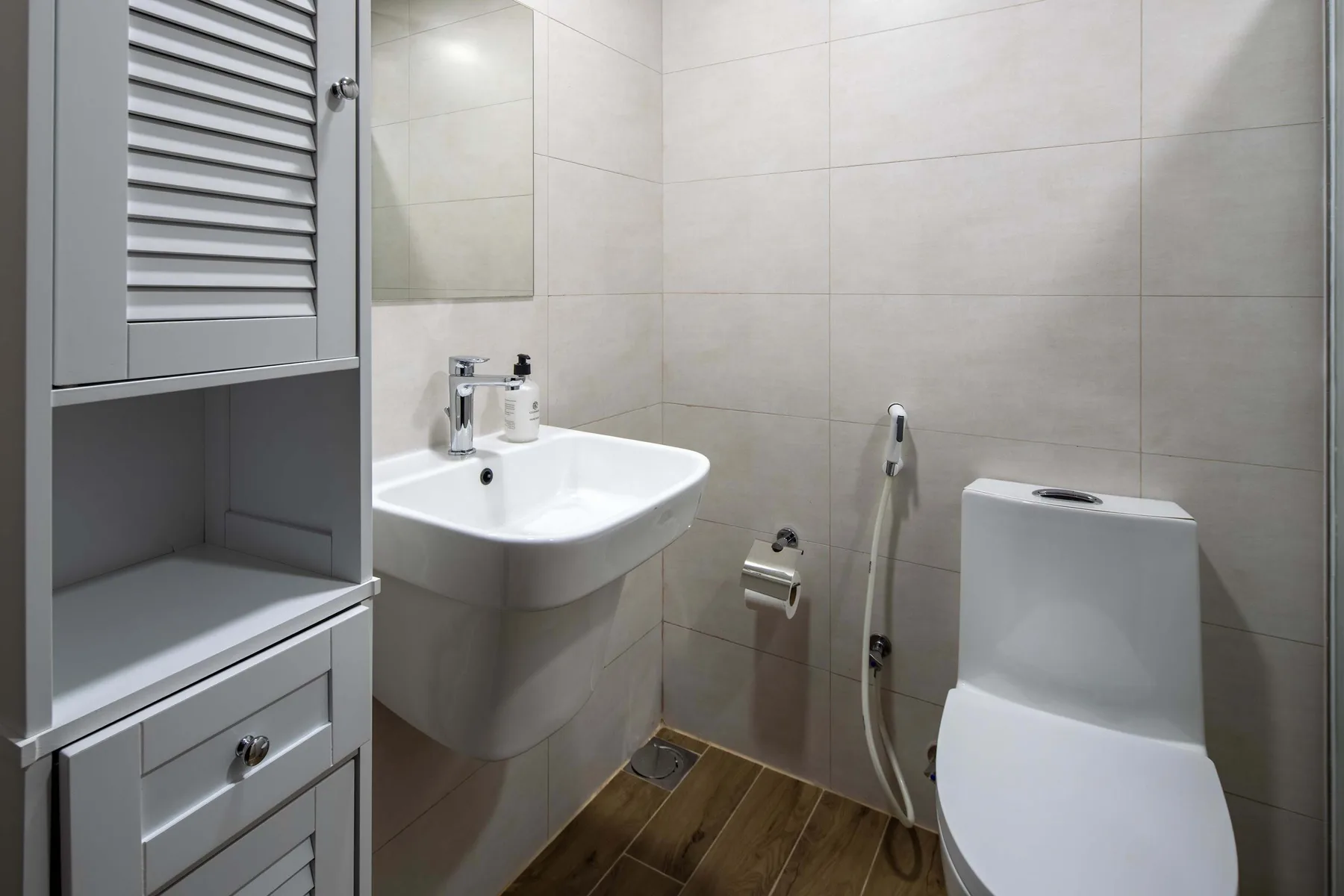 Un baño alicatado con lavabo, inodoro y ducha higiénica de mano.