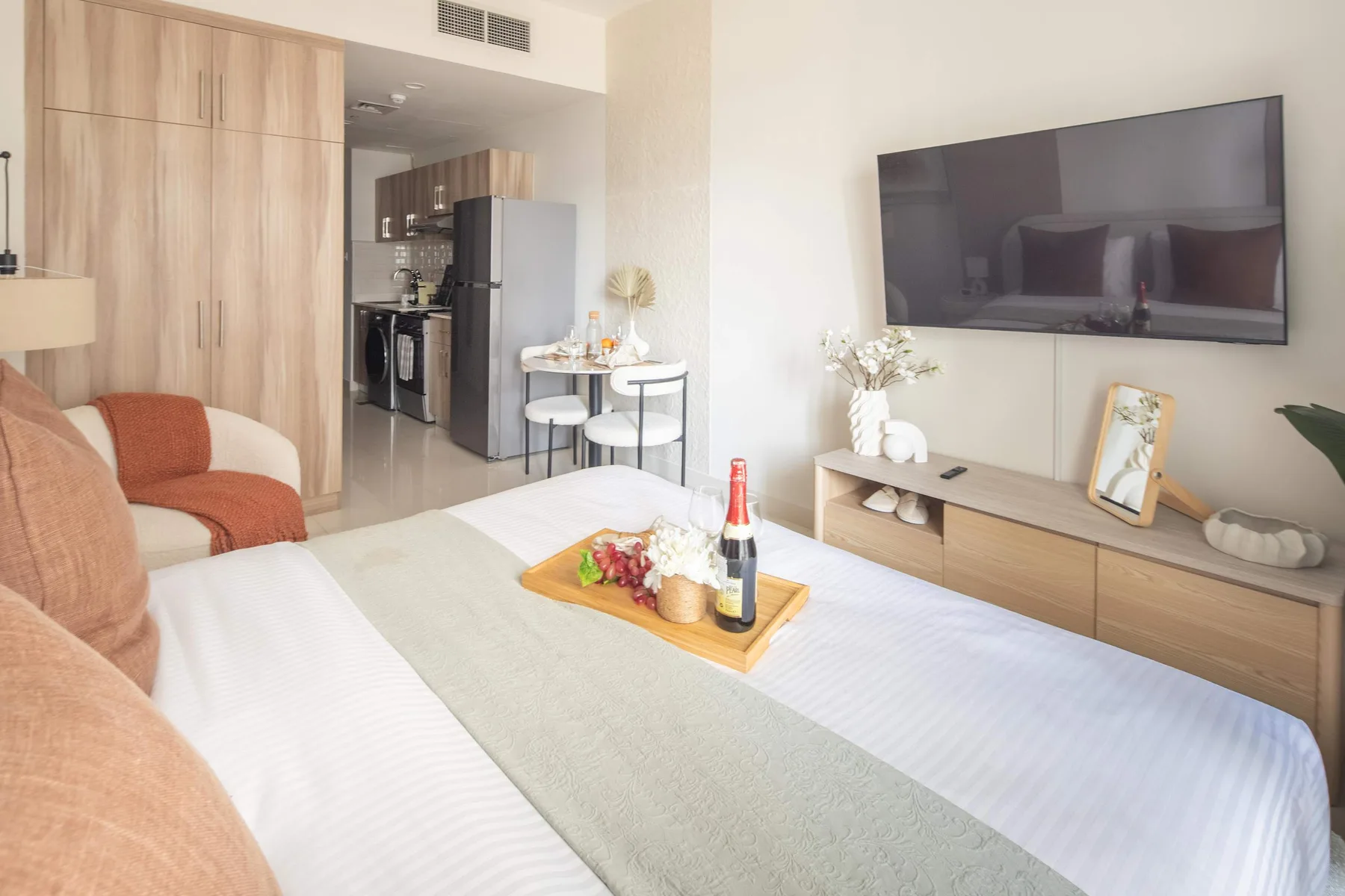 Una luminosa sala de estar con cama, asientos y un televisor montado en la pared.