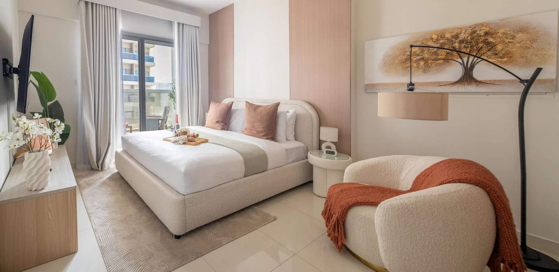 Un dormitorio con una cama tendida y un sillón color crema cubierto con una manta naranja.