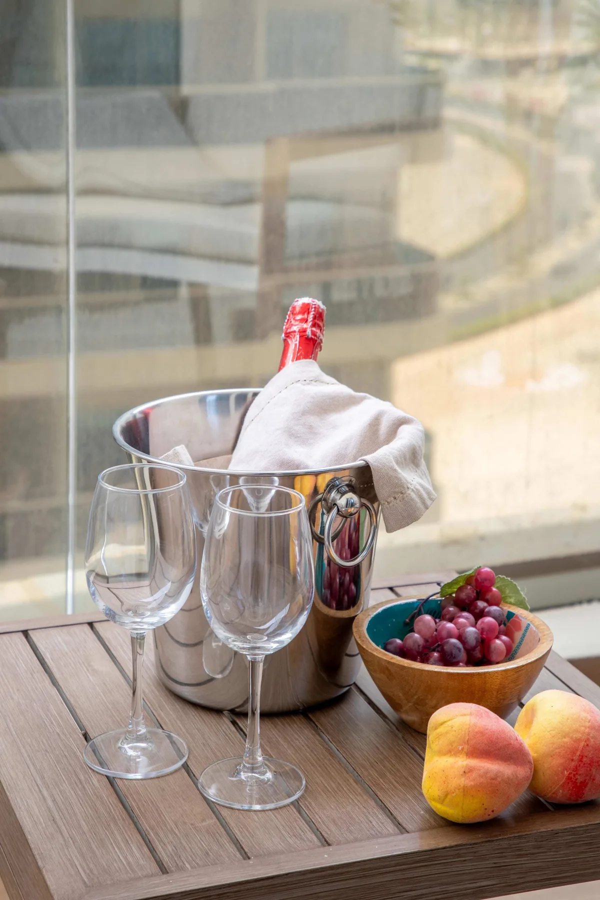 Una mesa muestra una botella fría, copas de vino, uvas y duraznos.