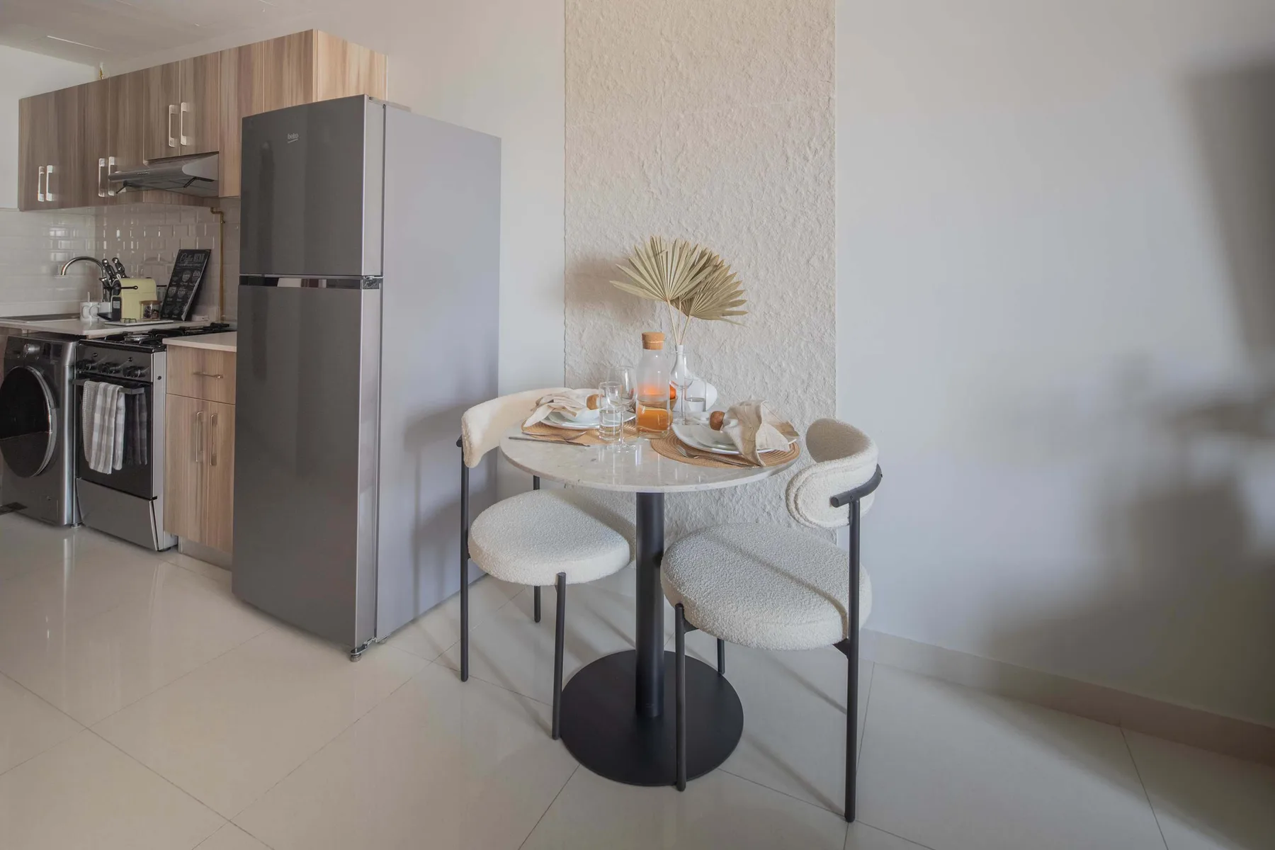 Una pequeña cocina y zona de comedor con una mesa redonda preparada para comer.