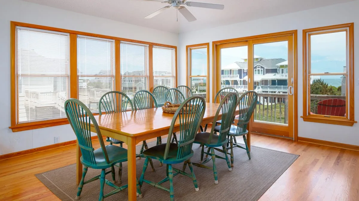 A dining area with a wooden table and green seating beside large windows.