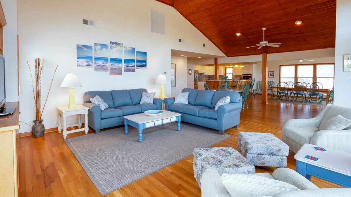 A bright living room with blue seating, a coffee table, and a dining area beyond.