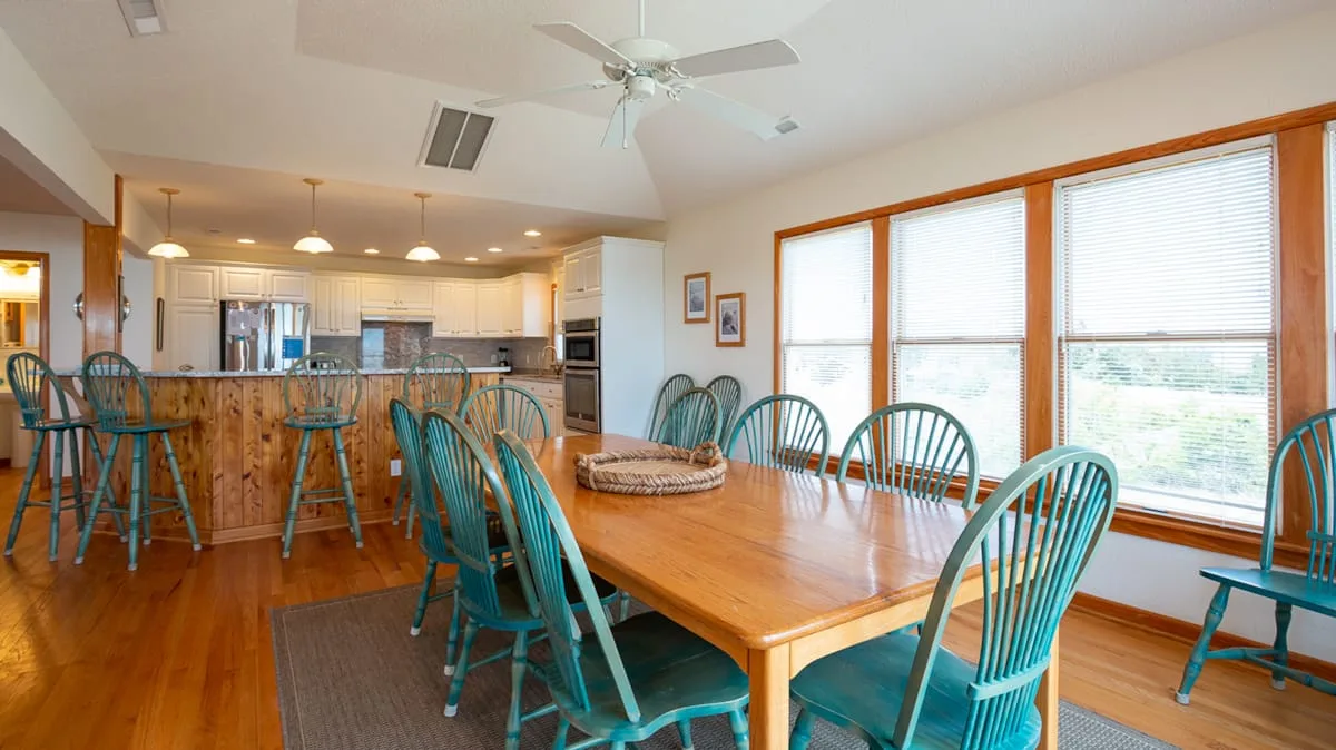 A dining area with a wooden table and large windows beside an open kitchen.