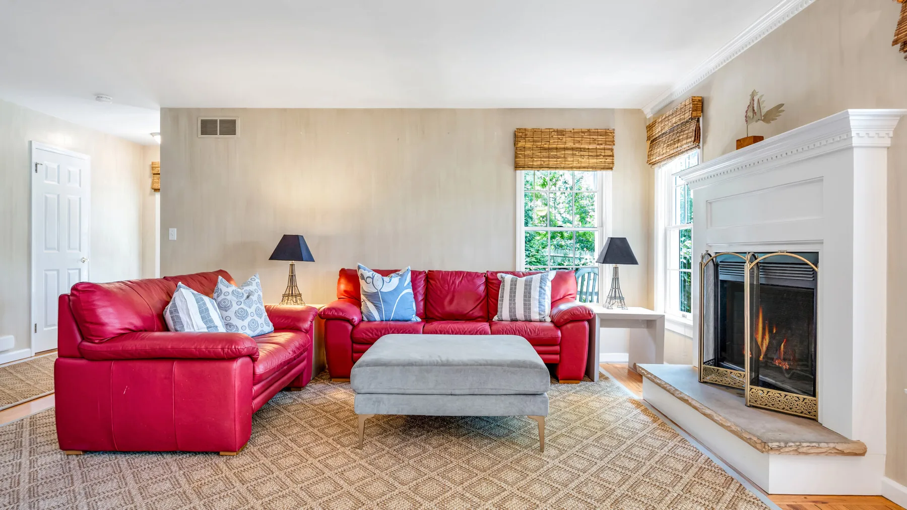 Una sala de estar con asientos rojos, una otomana central y una chimenea.