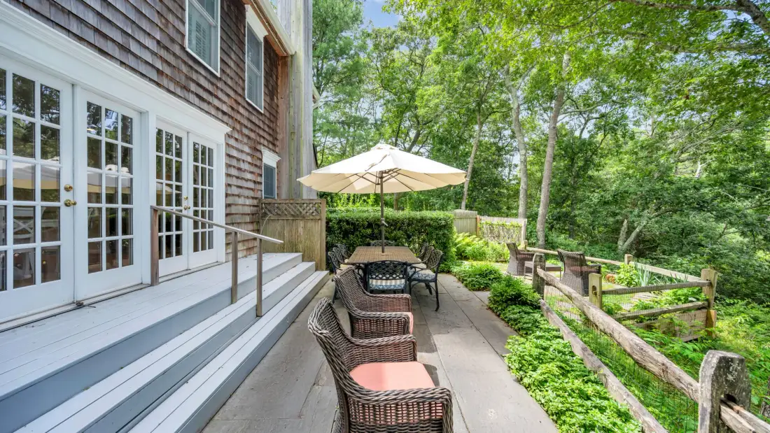 An outdoor deck with seating and an umbrella beside a wooded yard.