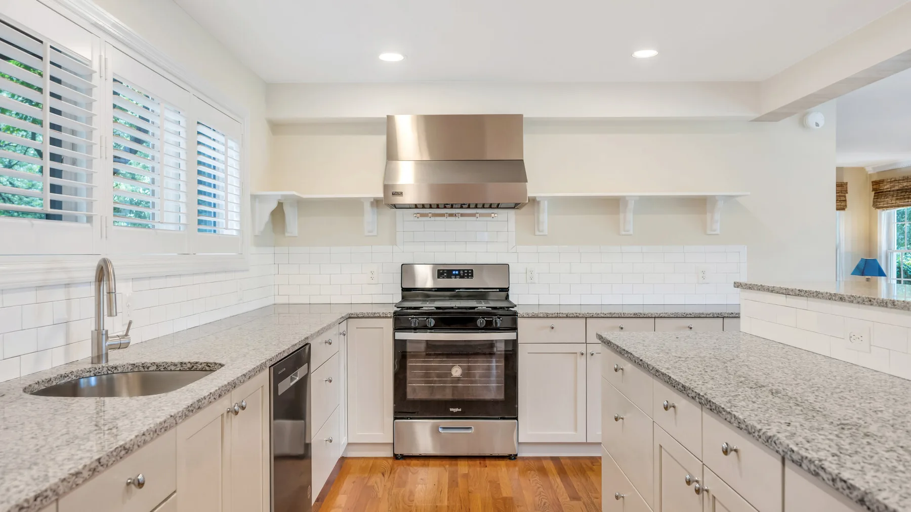 Una cocina luminosa con gabinetes blancos, encimeras de piedra y una estufa de acero inoxidable.