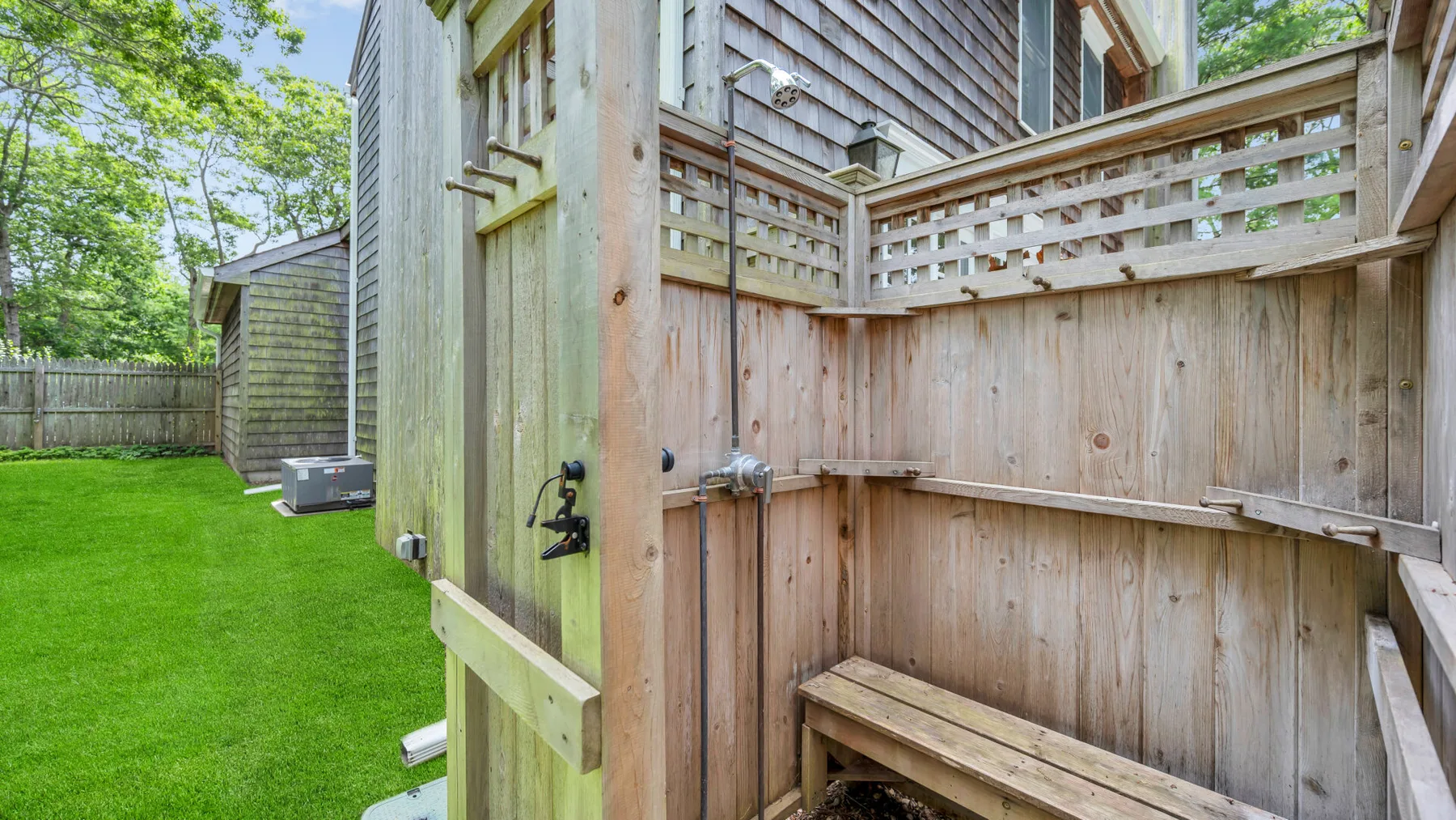 Una ducha exterior de madera con un banco junto a un patio cubierto de césped.