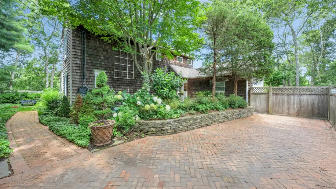 Una entrada de ladrillos pasa junto a un jardín paisajístico y llega a una casa.