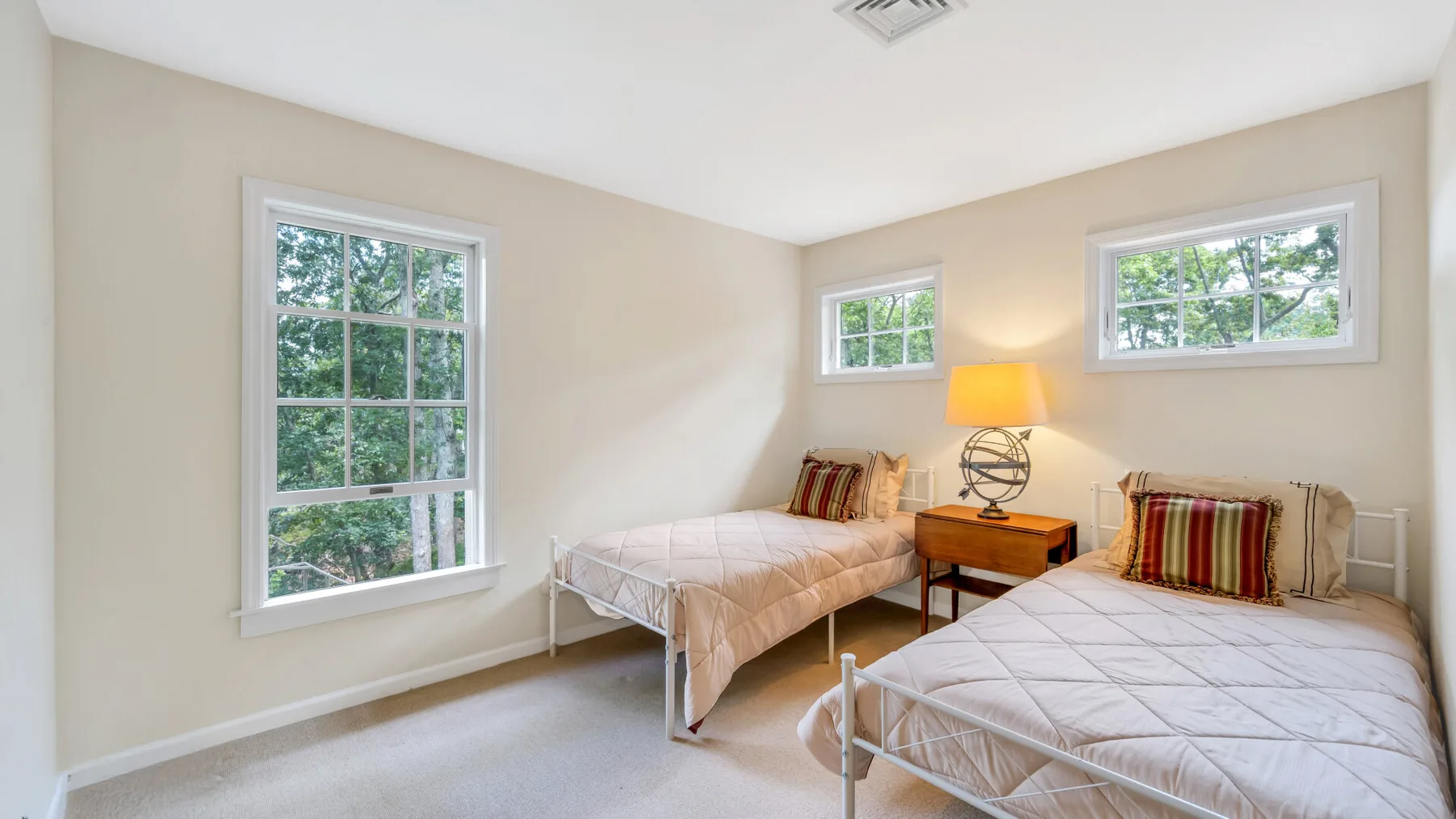Un dormitorio luminoso con dos camas, una lámpara de noche y varias ventanas.