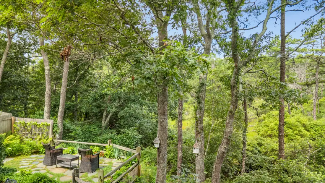 Un patio en un jardín arbolado con asientos al aire libre y una barandilla.