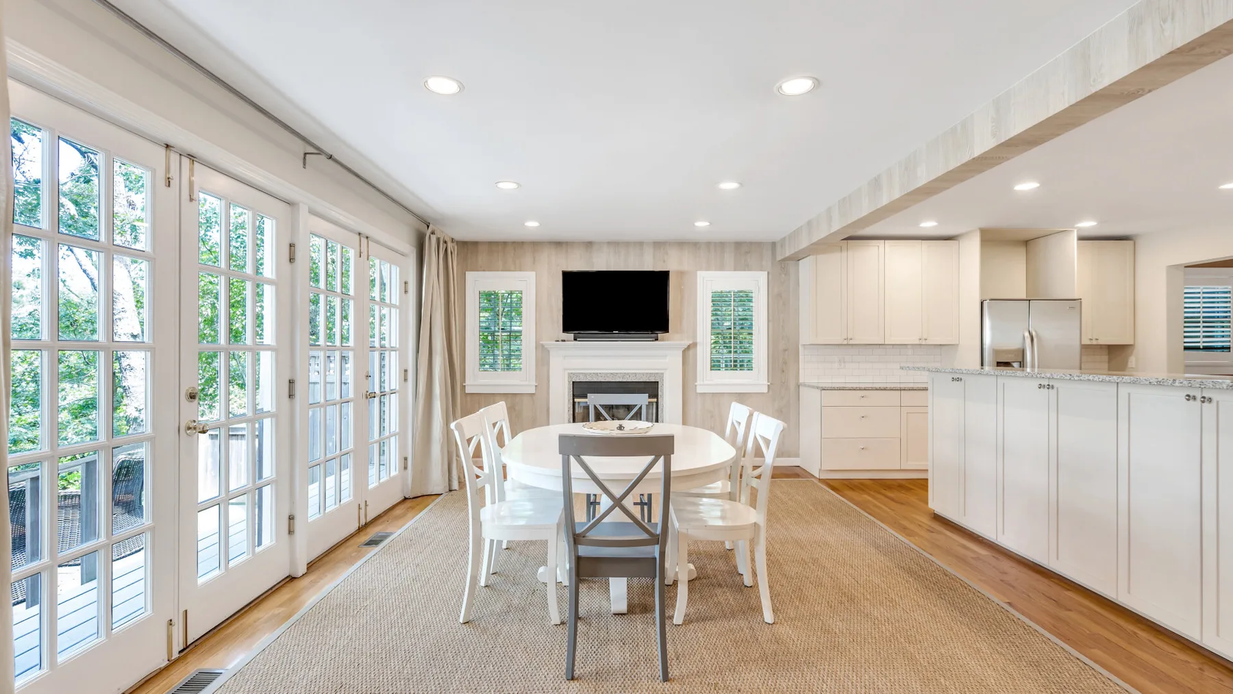 Un comedor luminoso con una mesa junto a grandes ventanas y una cocina.