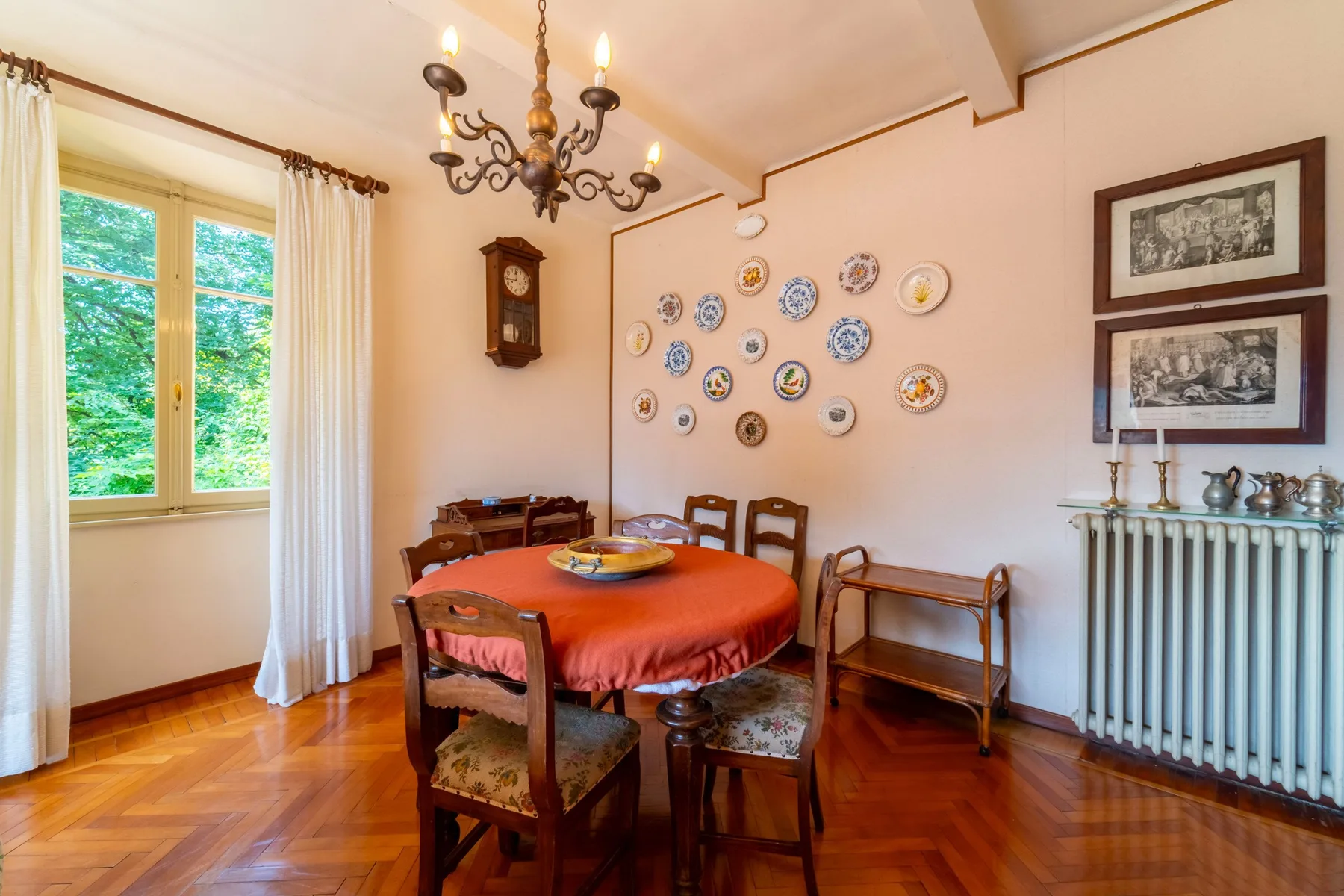A dining room with a wooden table, wall decorations, and a window overlooking greenery.