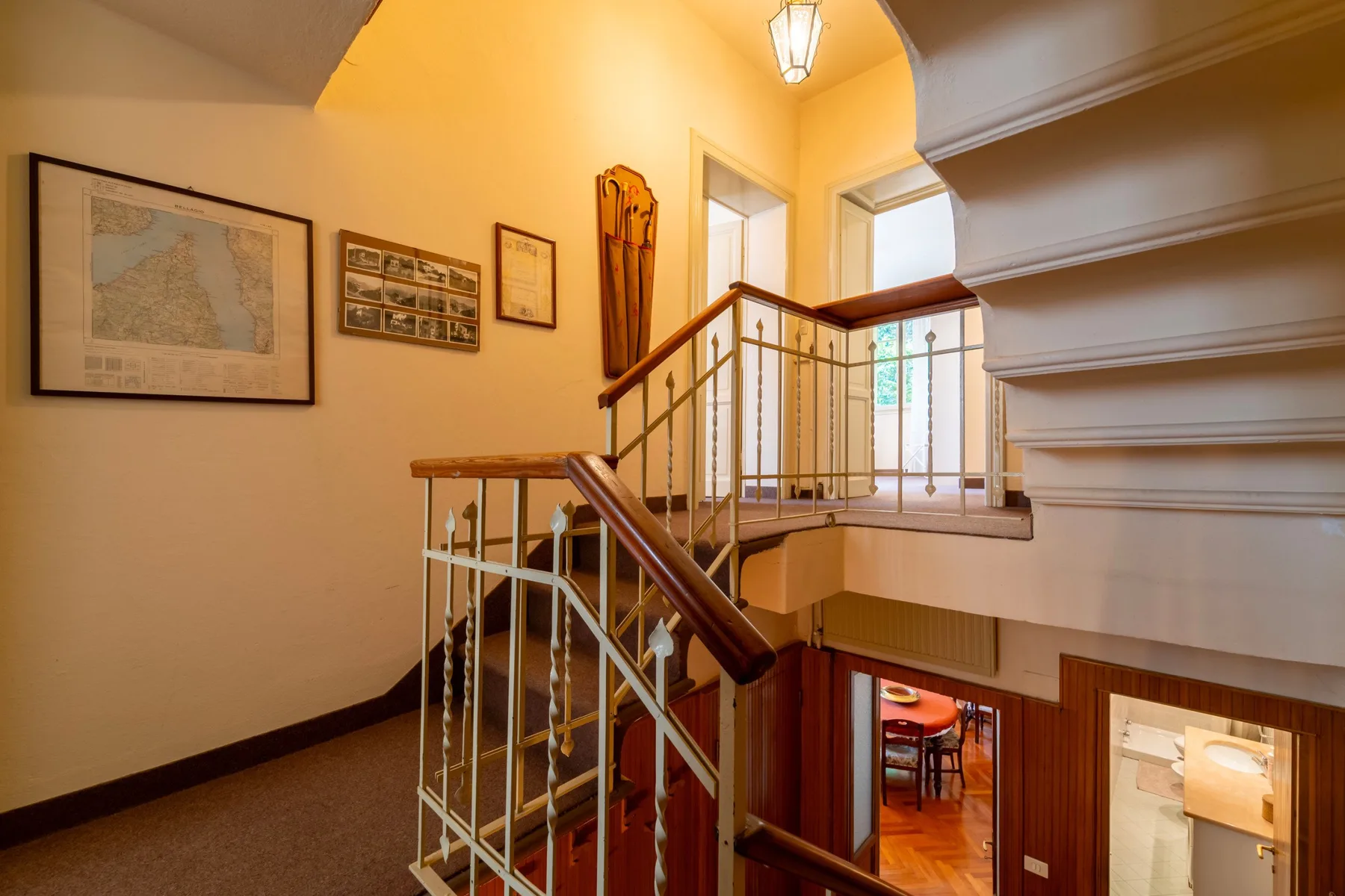 A warmly lit interior staircase and landing with framed artwork on the wall.
