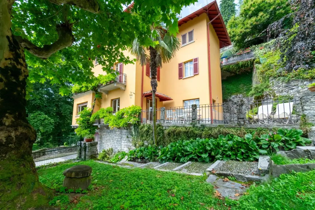 A yellow house stands beside a lush garden and stone steps.
