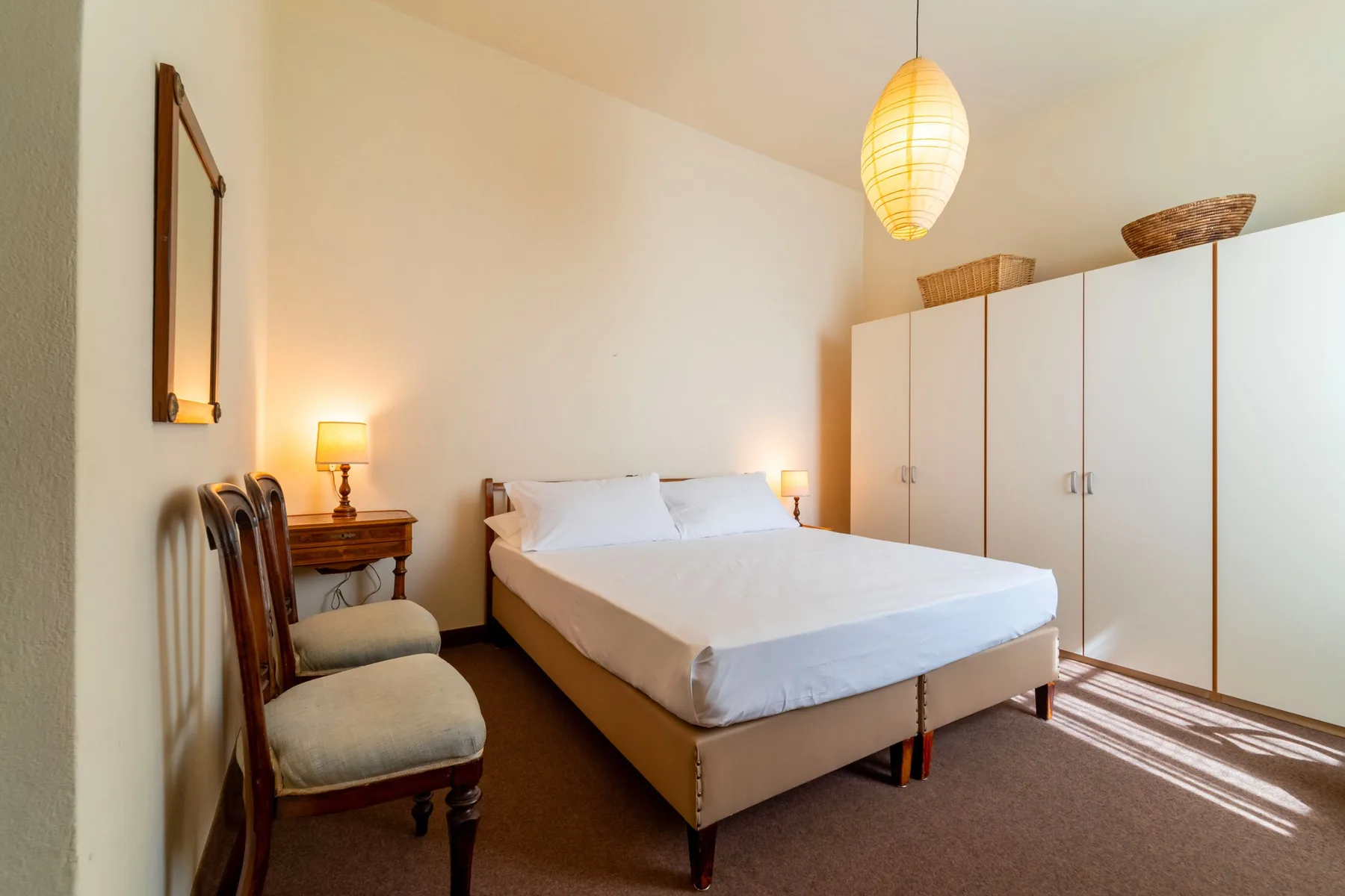 A bedroom with a bed, bedside table, and white wardrobes.