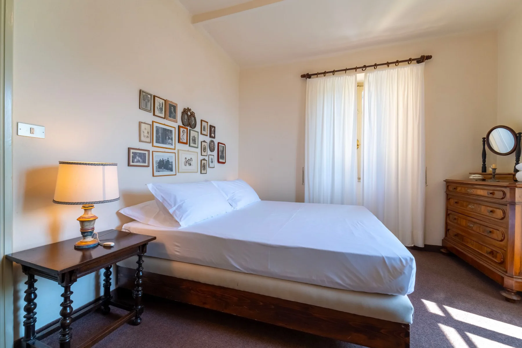A bedroom with a neatly made bed, bedside table, and framed pictures on the wall.