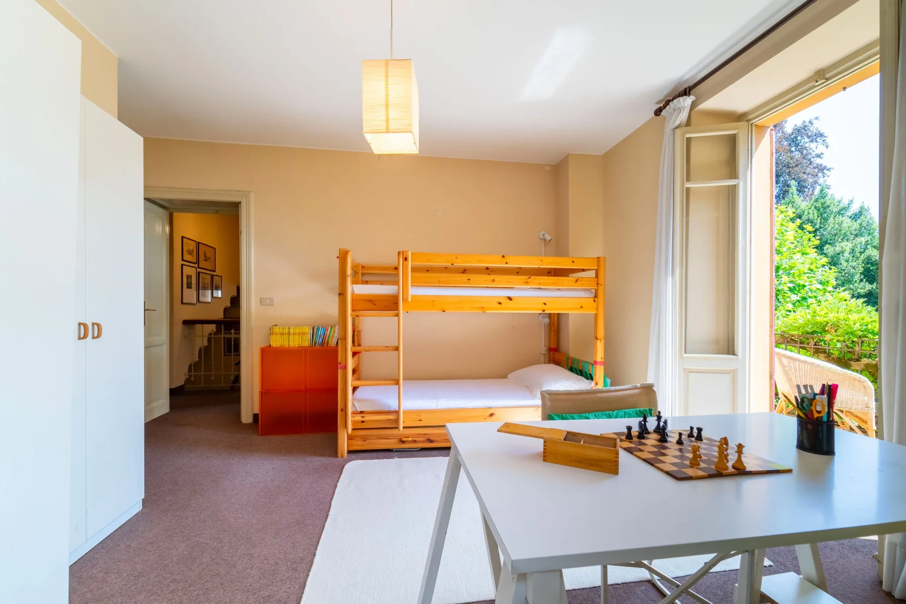 A bright bedroom with wooden bunk beds and a desk beside an open window.