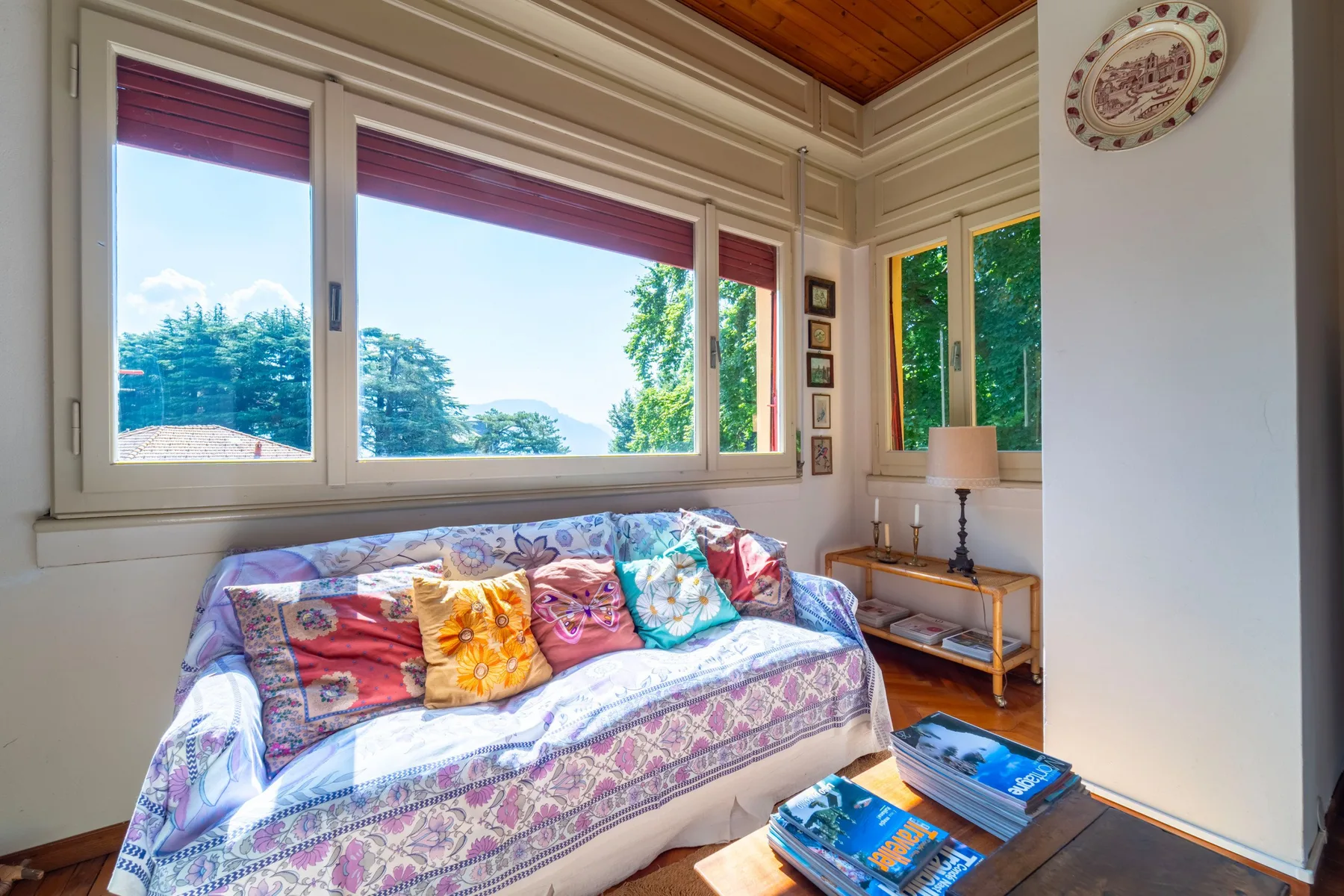 A bright living room with patterned seating beneath large windows.