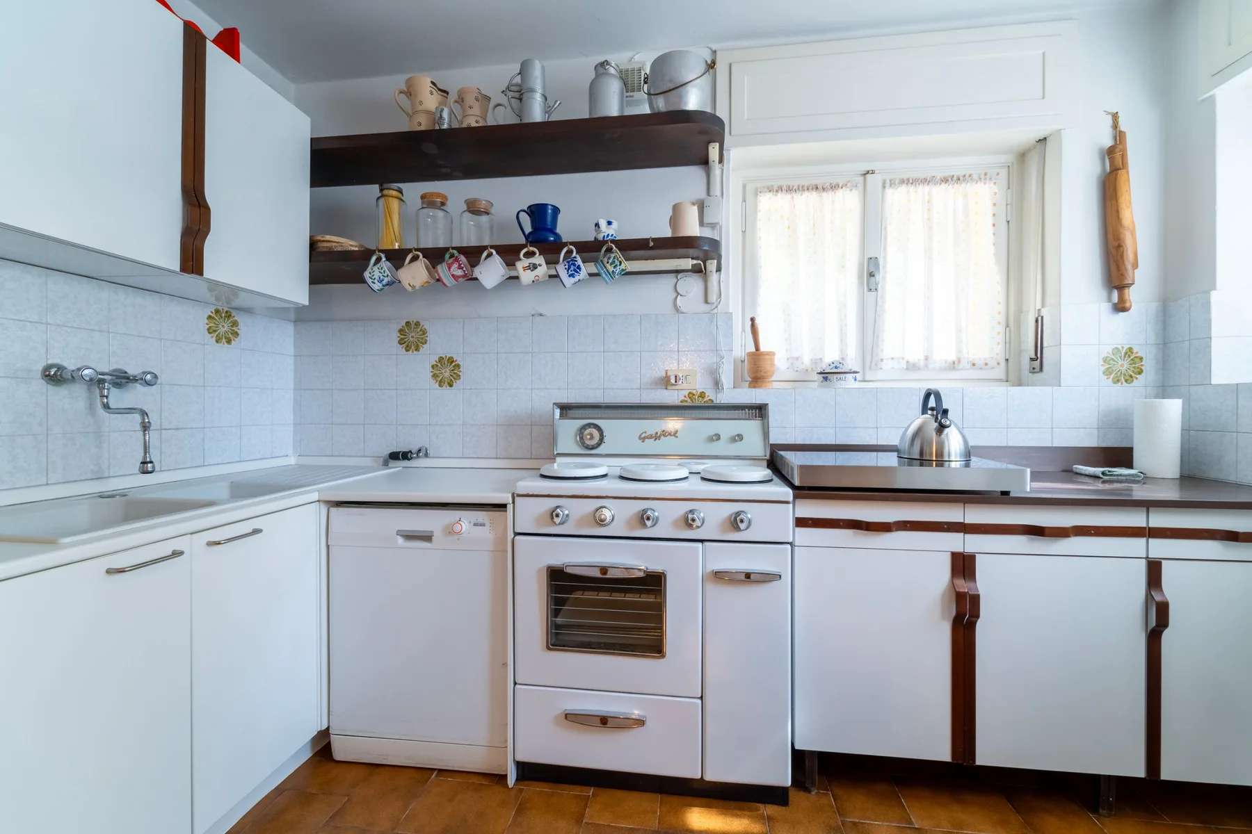 A bright kitchen with white cabinets, a stove, and a window over the counter.
