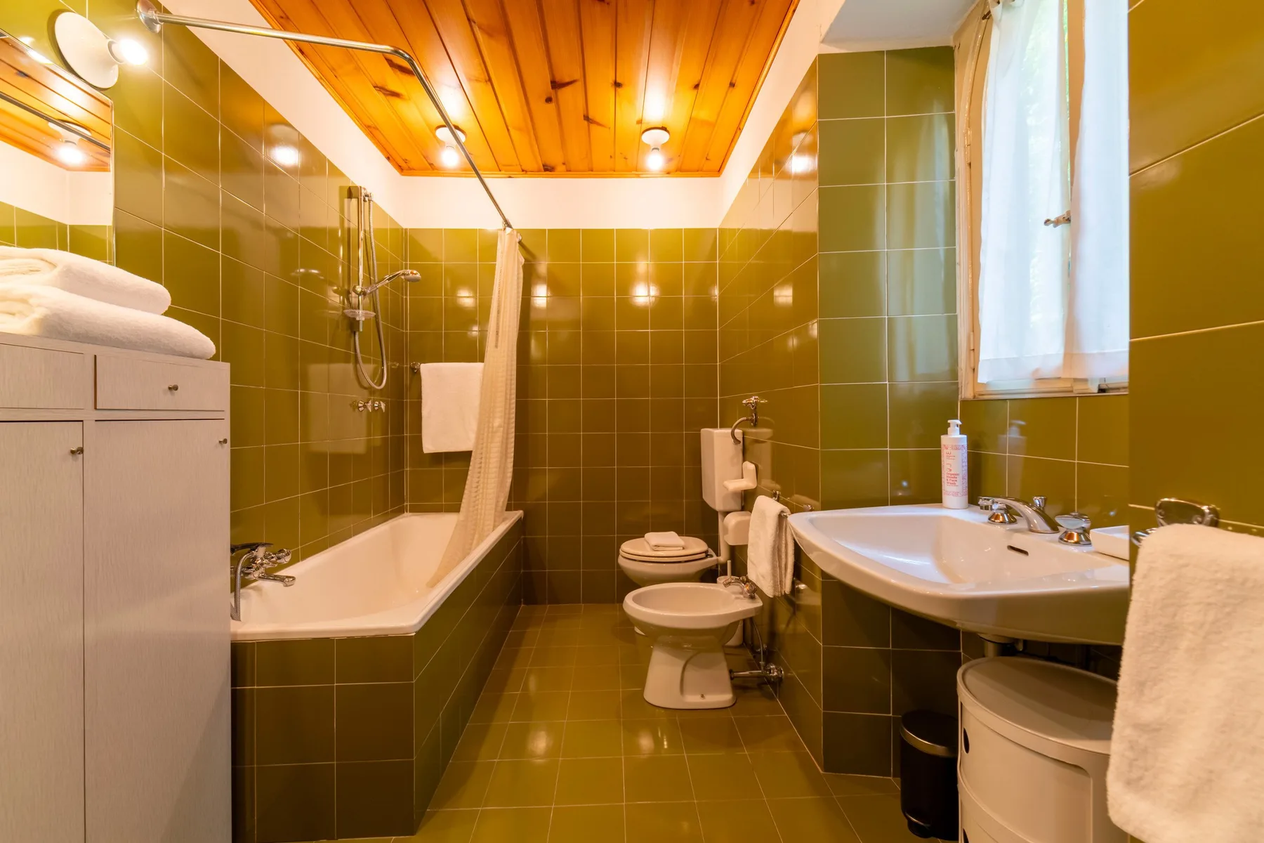 A tiled bathroom with a bathtub, toilet, and sink beneath a wood-paneled ceiling.