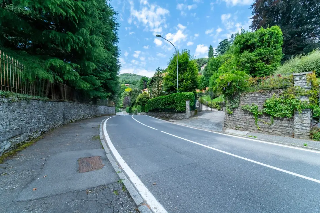 A curving road runs between stone walls and leafy greenery.